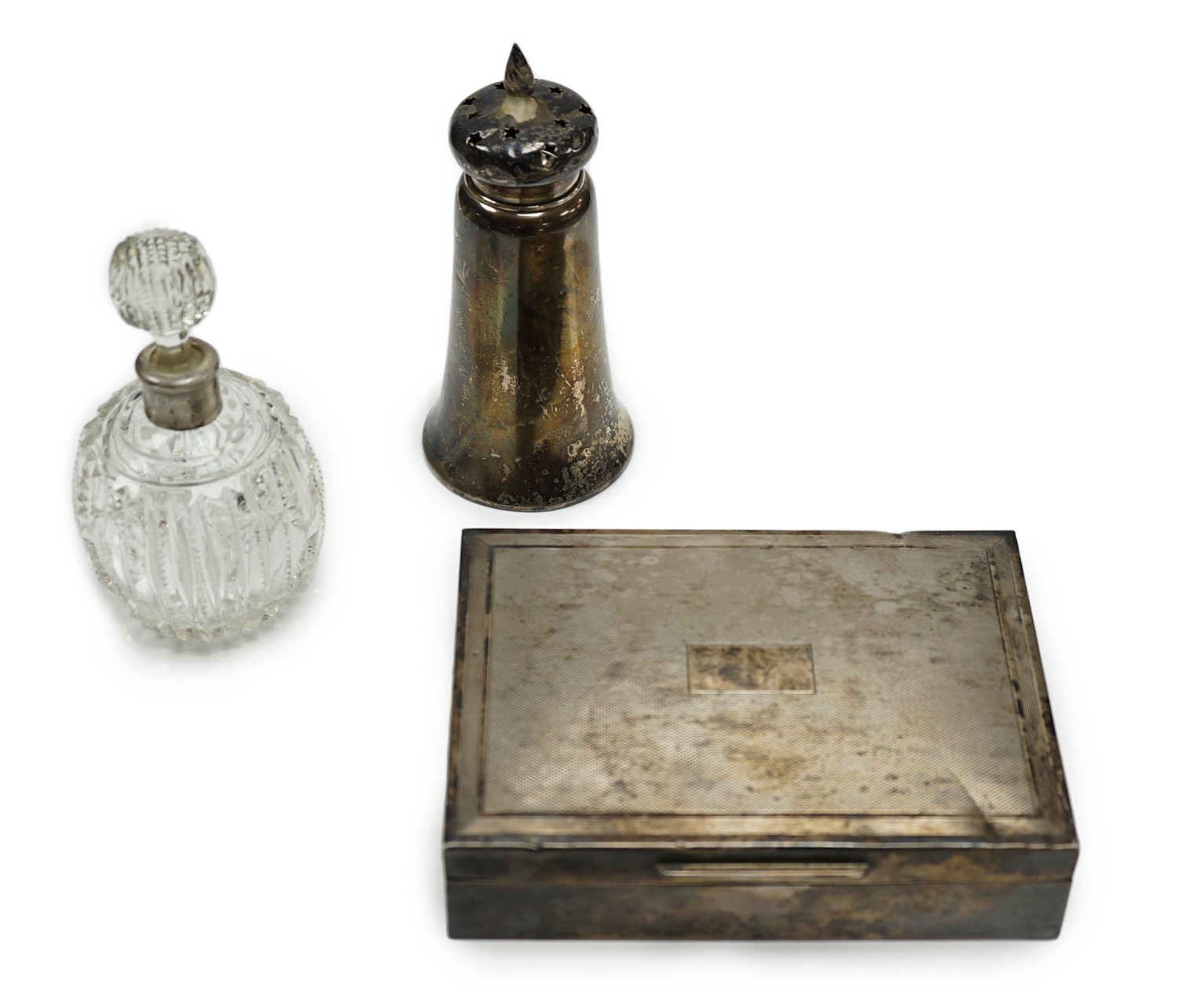 A 1970's engine turned silver mounted rectangular cigarette box, a silver mounted glass sugar caster and a similar scent bottle.                                                                                            