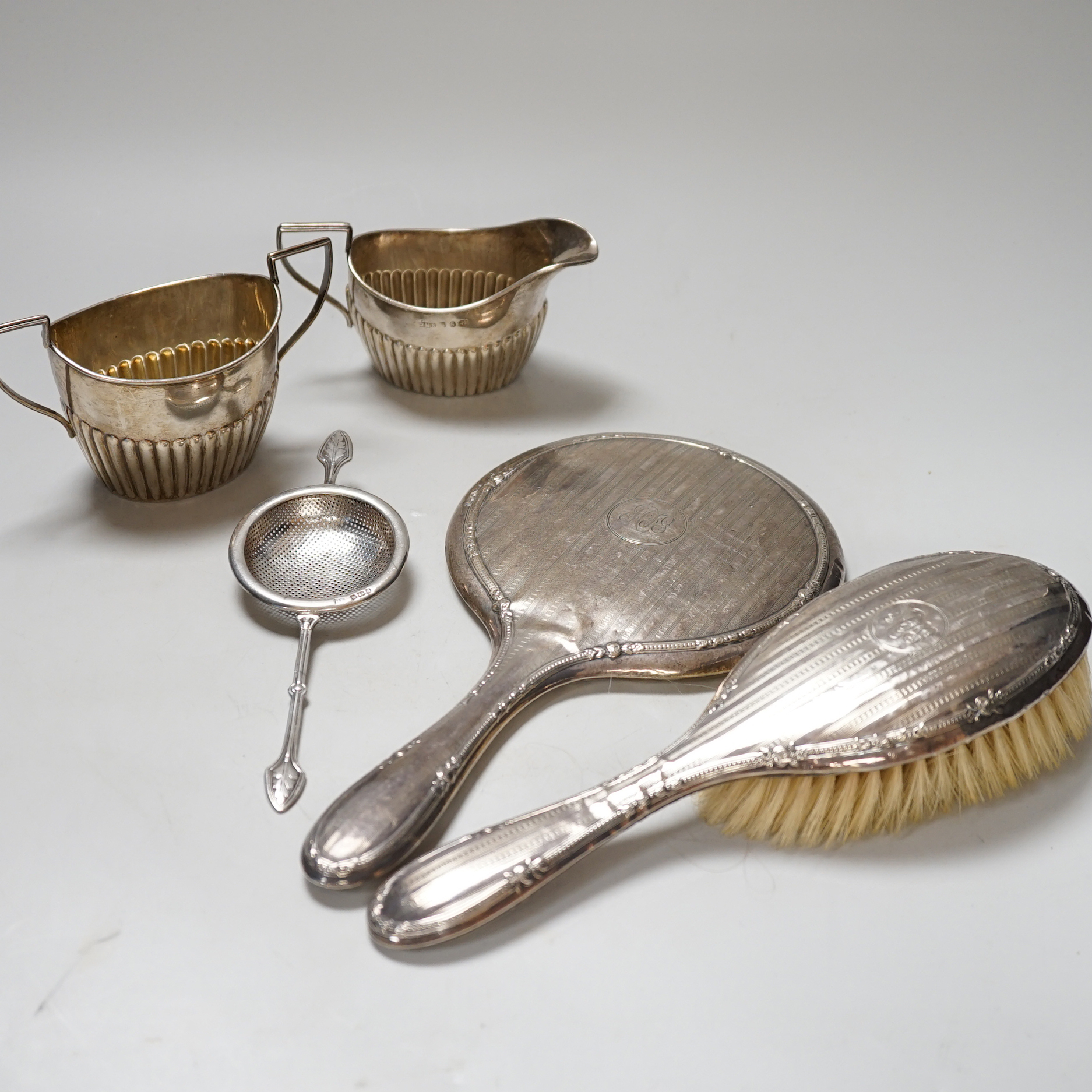 A late Victorian silver bachelor's cream jug with matching sugar bowl, Birmingham 1892, 160 grams, a George V tea strainer, 47 grams and a silver mounted hair brush and hand mirror                                        