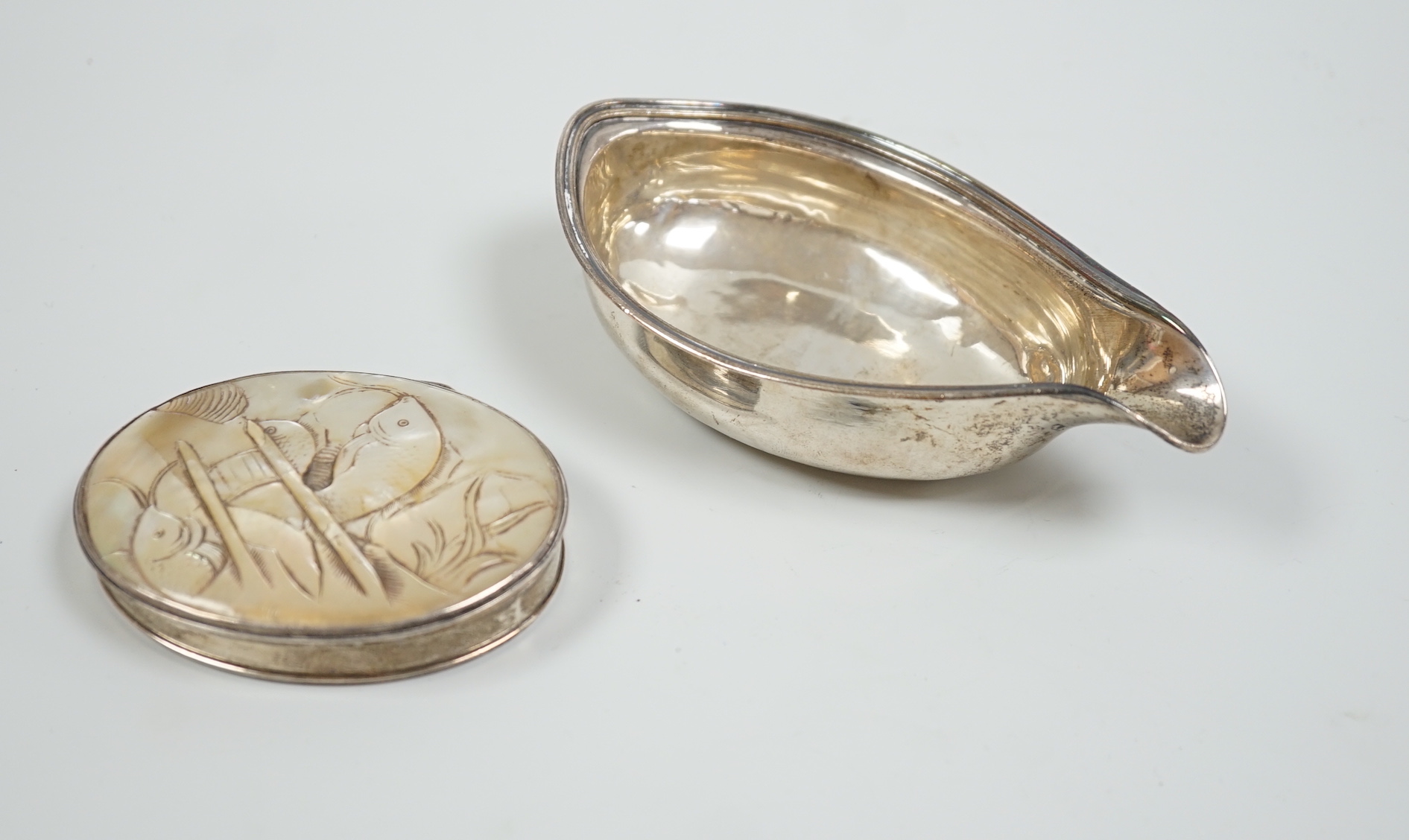 A late George III silver pap boat, London, 1817, 12.8cm, together with a 19th century white metal oval snuff, with inset mother of pearl cover, carved with fish, 8cm.                                                      