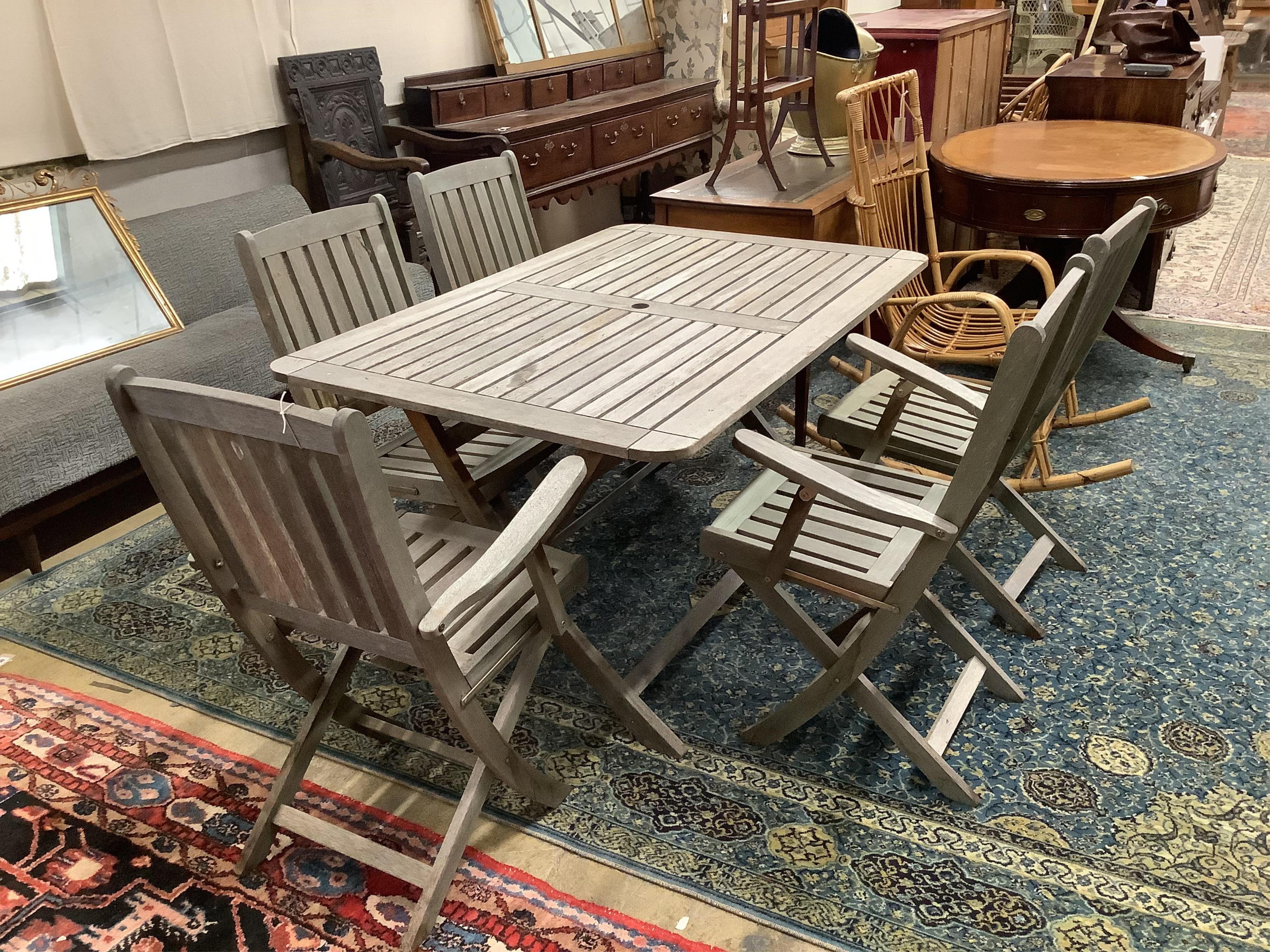 A weathered teak rectangular folding garden table, width 140cm, depth 90cm, height 72cm, and five folding teak garden chairs, two with arms. Condition - fair                                                               