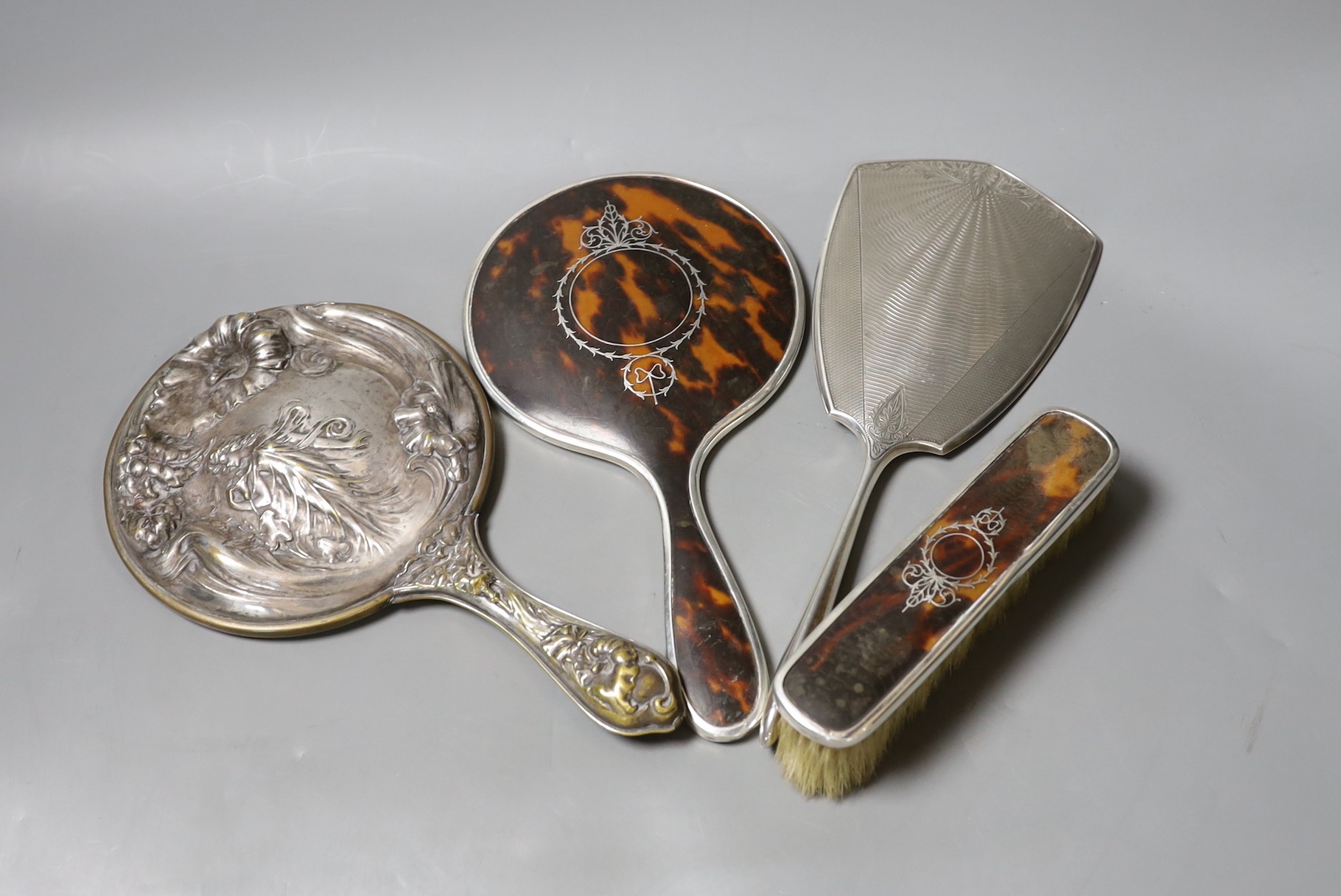 A George V silver and tortoiseshell mounted hand mirror and clothes brush, one other silver mounted hand mirror and a plated hand mirror.                                                                                   