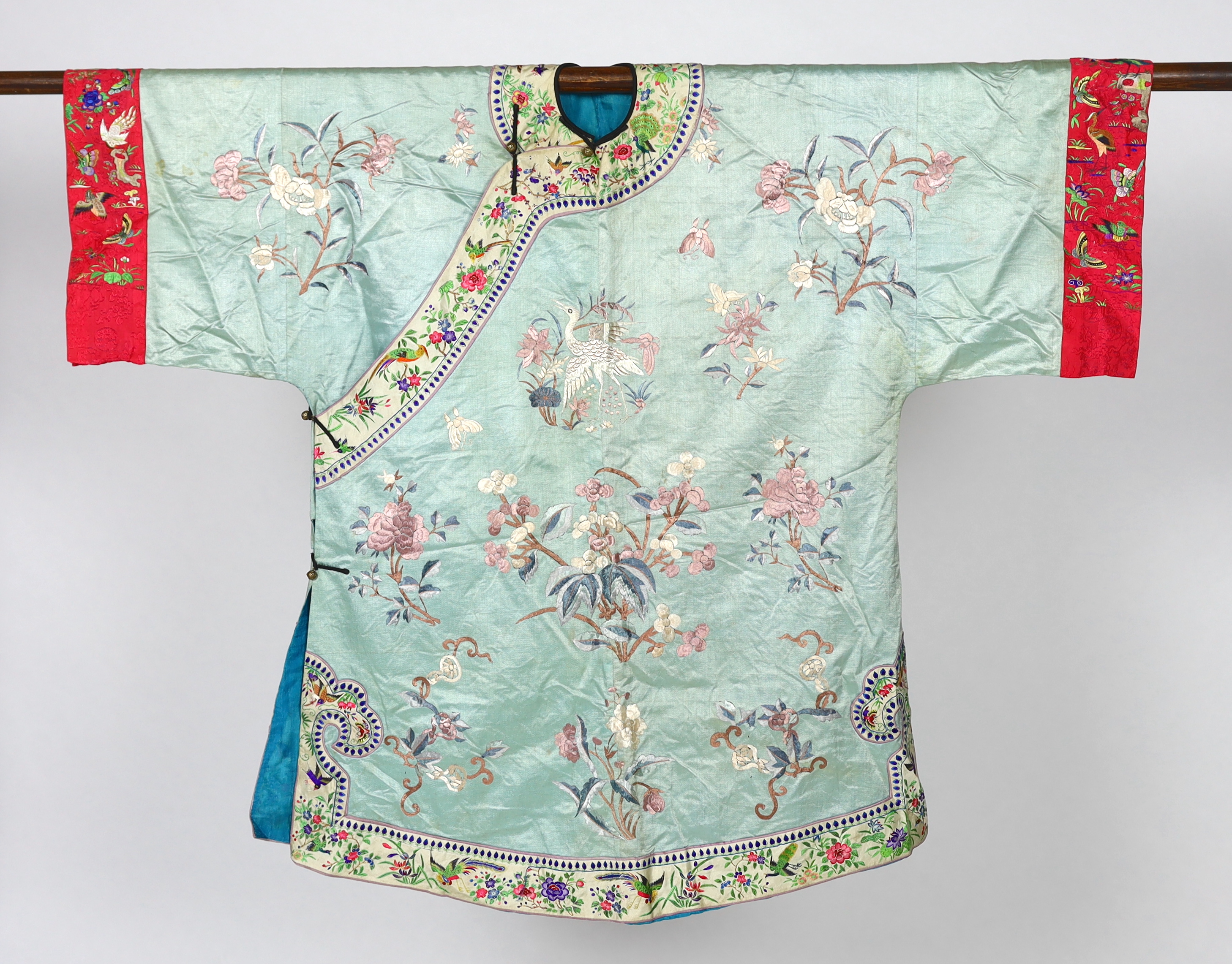 An early 20th century Chinese silk embroidered turquoise robe, embroidered in pastel silk with butterflies and flowers all over, polychrome embroidered braiding edged with lilac and bright pink sleeve bands embroidered w