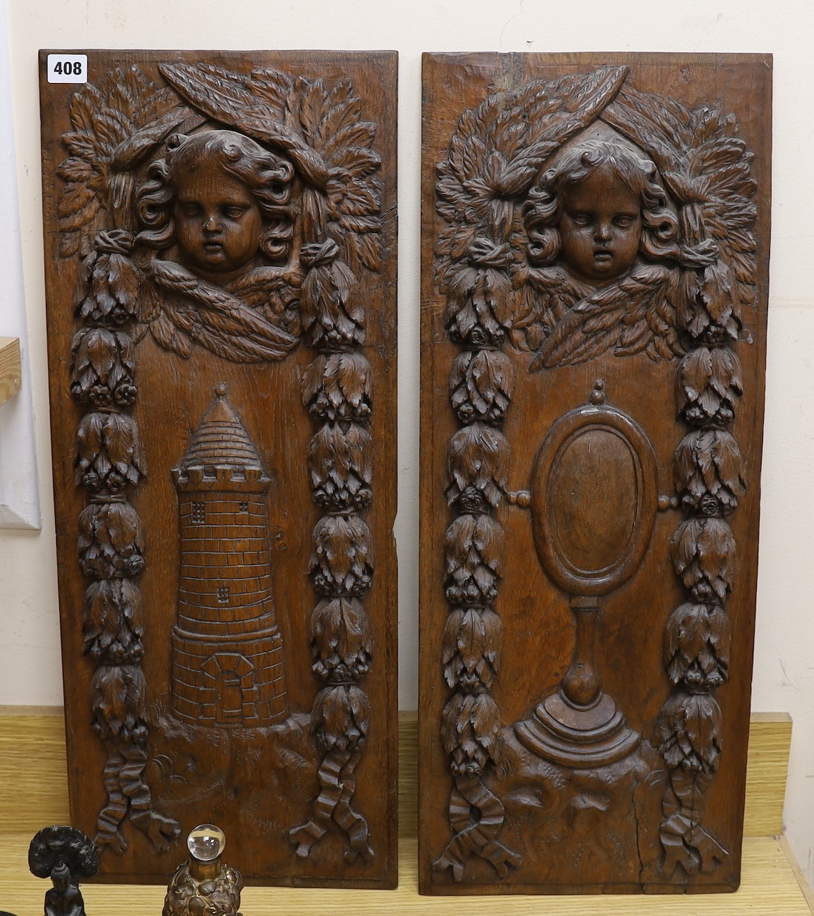 A pair of late 19th century continental carved oak panels, one detailing a lighthouse, the other a mirror, etc., 28.5 cms wide x 70 cms high                                                                                