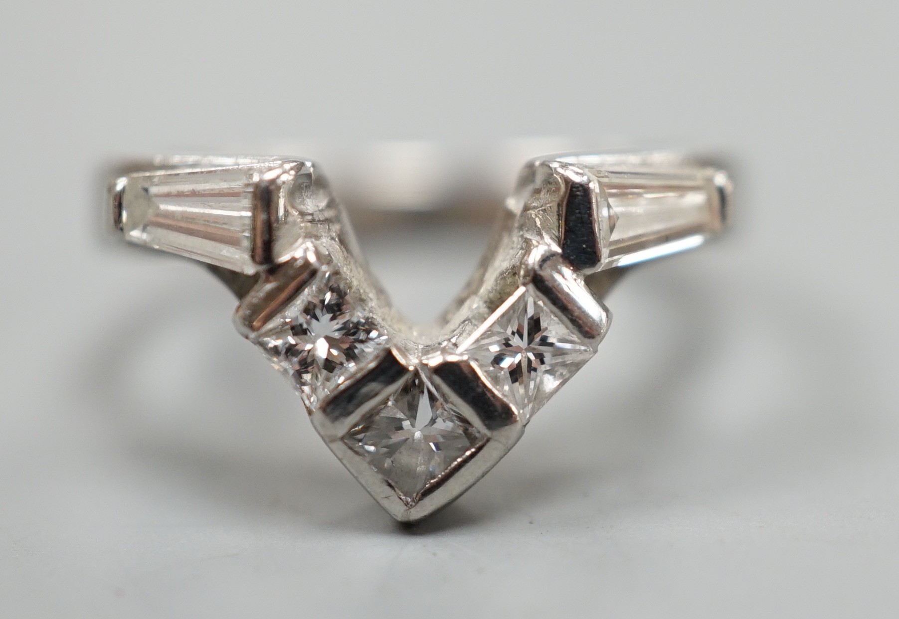 A modern white metal (stamped plat), two stone trapeze cut and three stone princess cut diamond set 'chevron' ring, size I, gross weight 5.3 grams.                                                                         