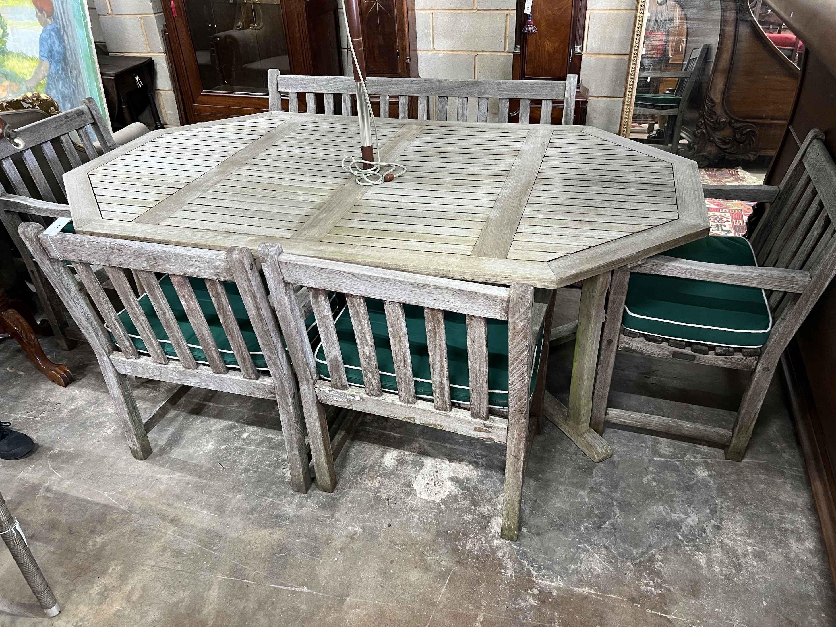 An Alexandra Rose weathered teak octagonal garden table, length 210cm, width 122cm, height 74cm, a bench, four elbow chairs with seat pads, and a green canvas parasol with cast metal base                                 