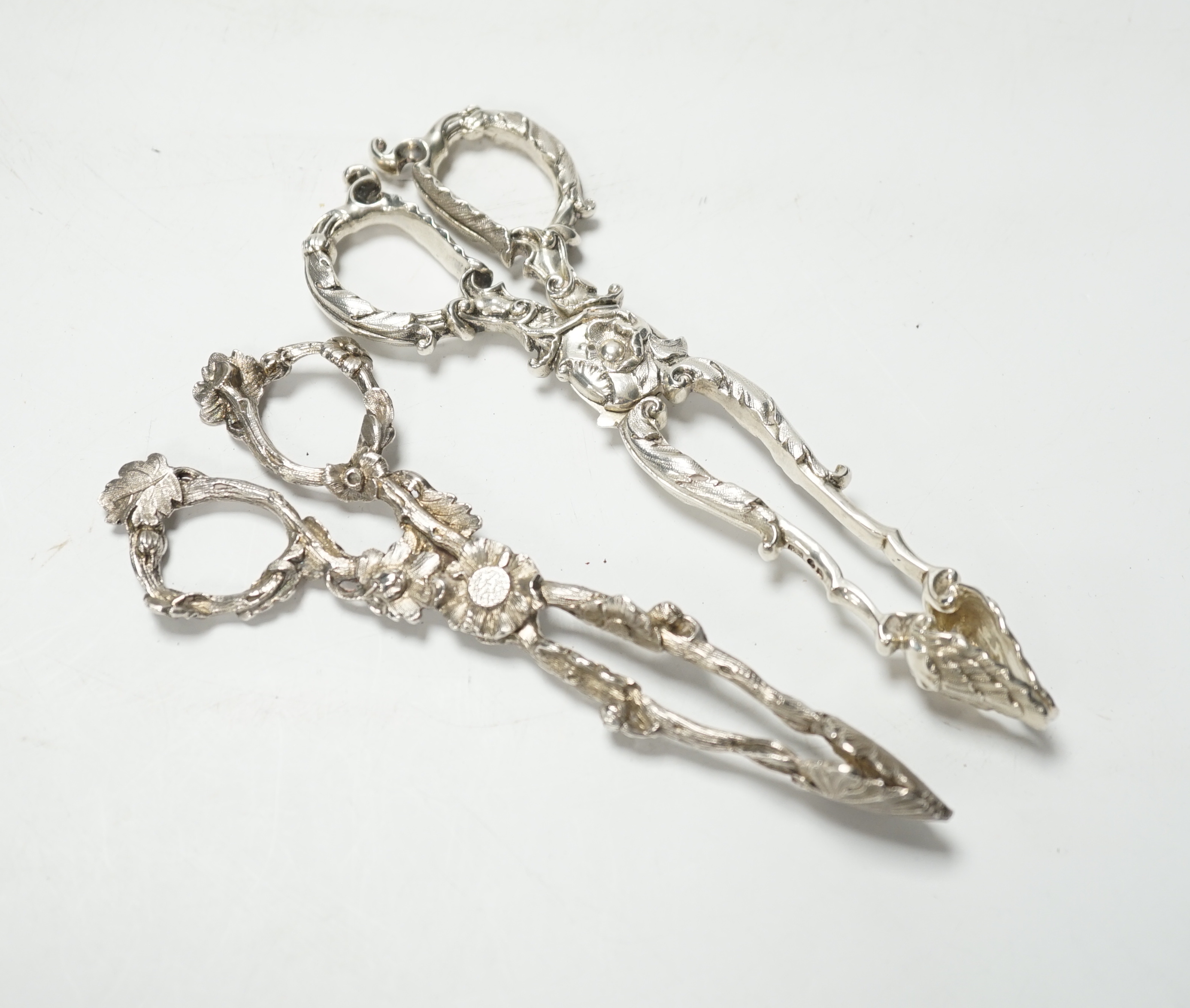 A pair of Victorian cast silver sugar tongs, of foliate design, by George Adams, London, 1871, 14.2cm and a pair of William IV cast silver sugar tongs, by Theobalds & Bunn, London, 1835, 15.4cm, 102 grams.               