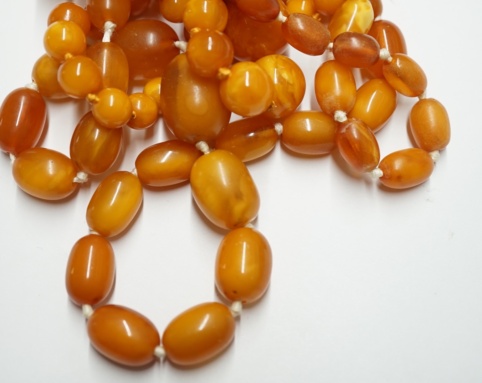 Two single strand graduated oval amber bead necklaces, longest 72cm, gross weight 63 grams. Condition - poor to fair                                                                                                        