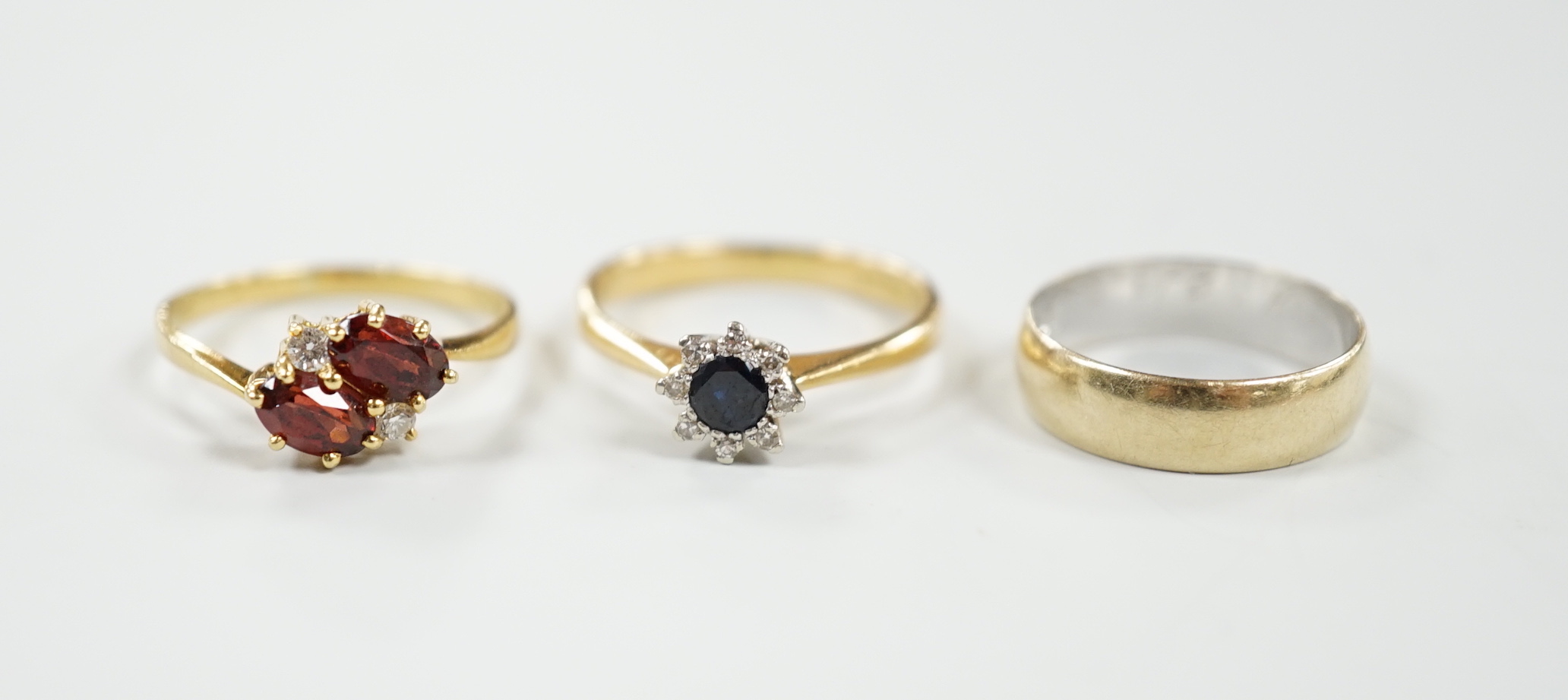 A modern 18ct gold, sapphire and diamond set cluster ring, size N/O, a similar 18ct gold, two stone garnet? and two stone diamond chip set crossover ring and an 18ct gold band, gross weight 8 grams.                      