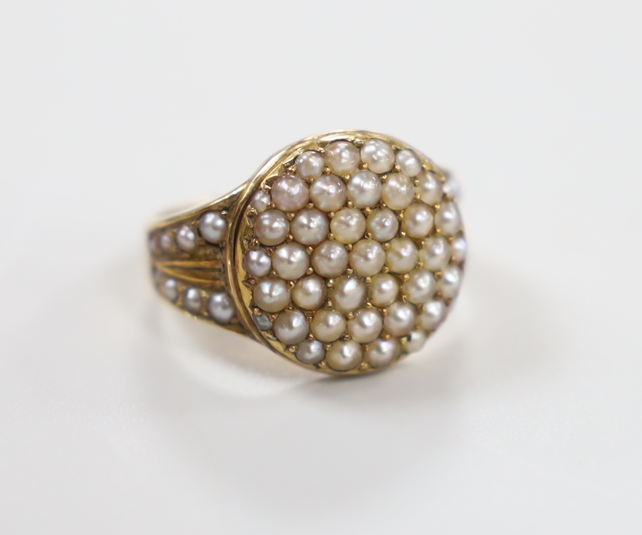 An Edwardian 15ct and seed pearl cluster set dress ring, with seed pearl set shoulders, size J/K, gross weight 5.6 grams, in original box.                                                                                  