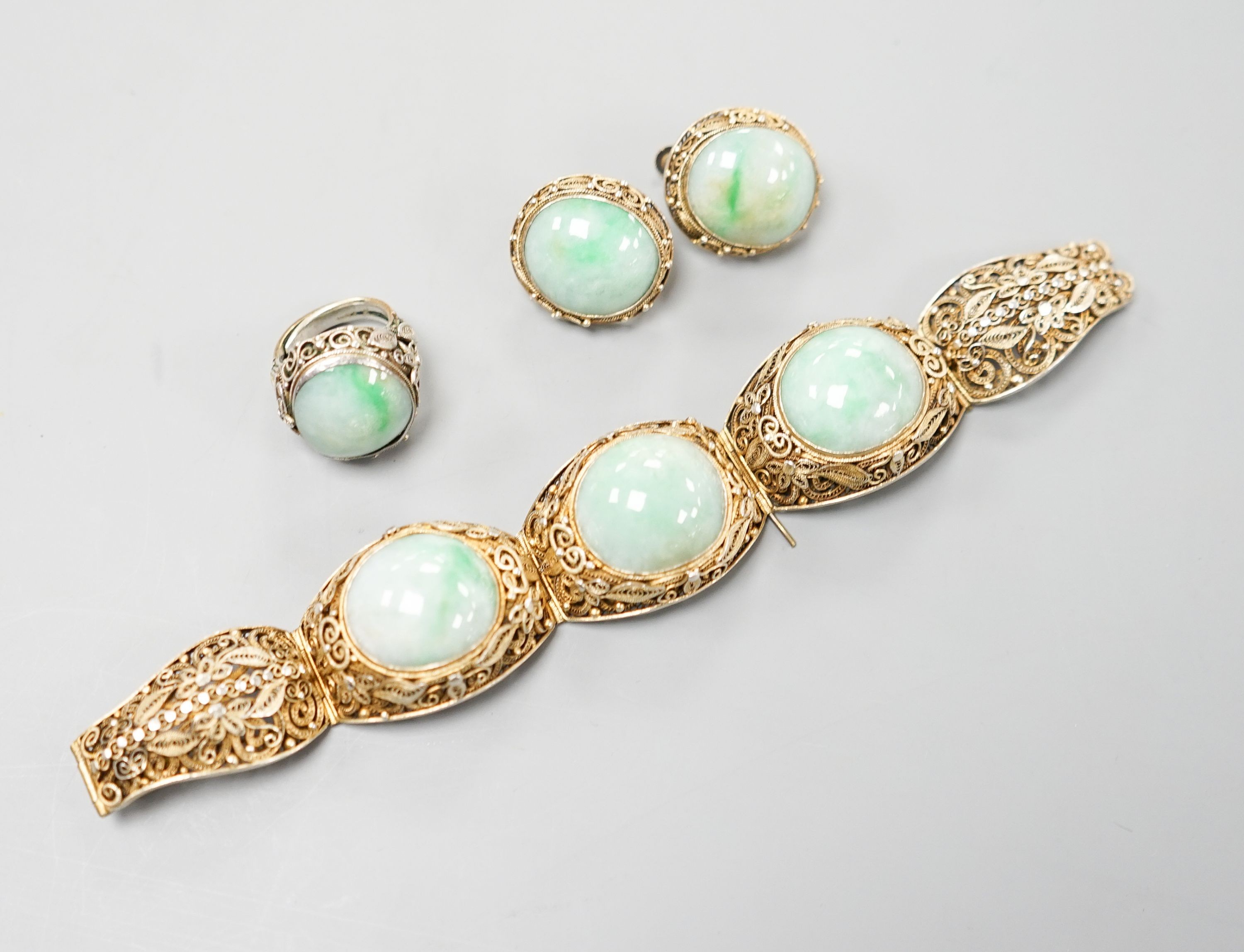 A Chinese filigree gilt white metal and three stone cabochon jade set bracelet, 17cm, a pair of matching ear clips, length 25mm and a similar white metal and cabochon jade set ring, size L.                               