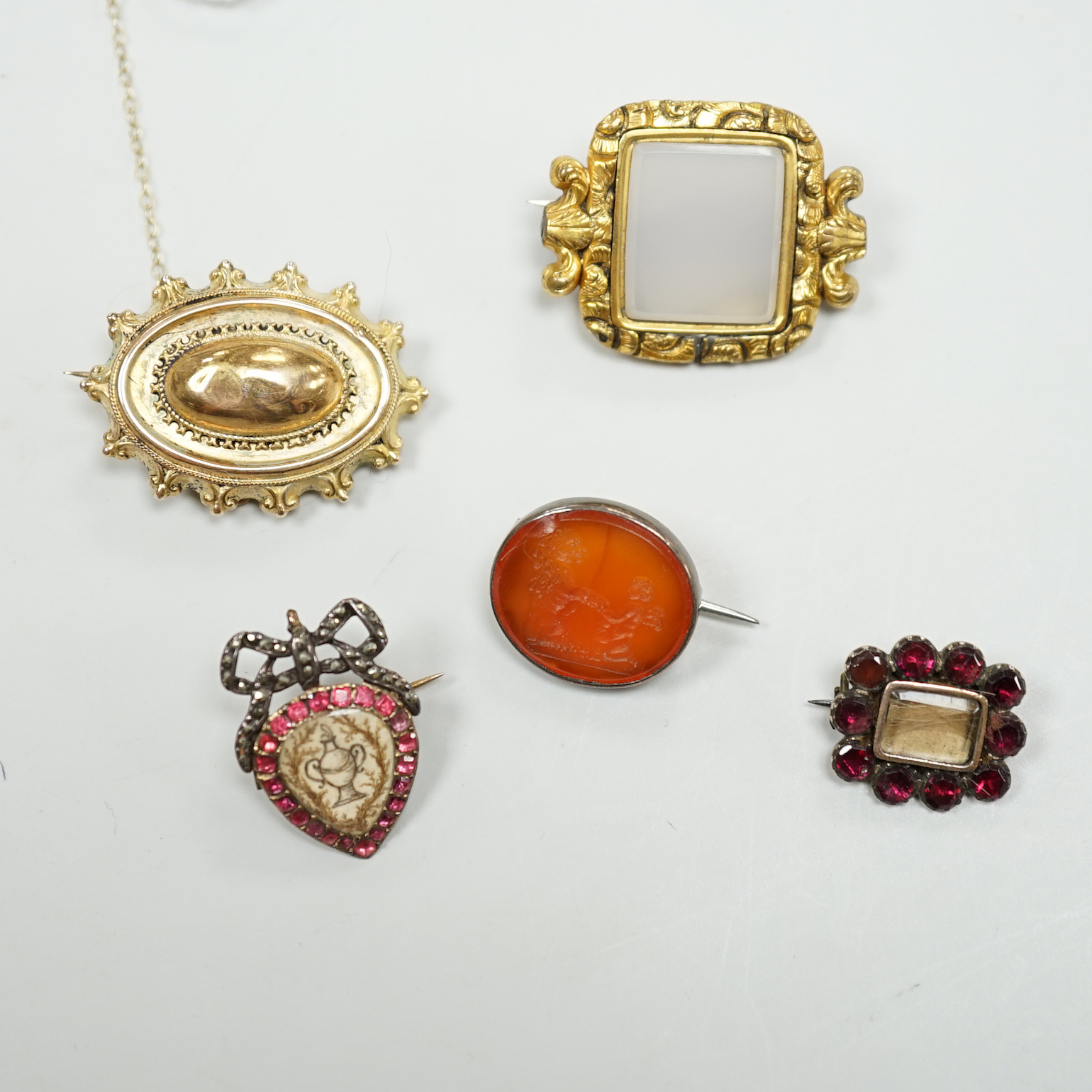 Five assorted antique brooches, comprising an early 19th century foiled ruby and hair work heart shaped brooch, 2.25cm, an early 19th century foiled garnet memorial brooch, 1.75cm, a Victorian unmarked gold oval brooch, 