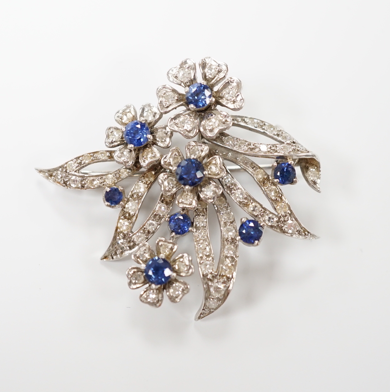 A white metal (stamped 18 plat), sapphire and diamond chip cluster set foliate brooch, 32mm, gross weight 11 grams.                                                                                                         