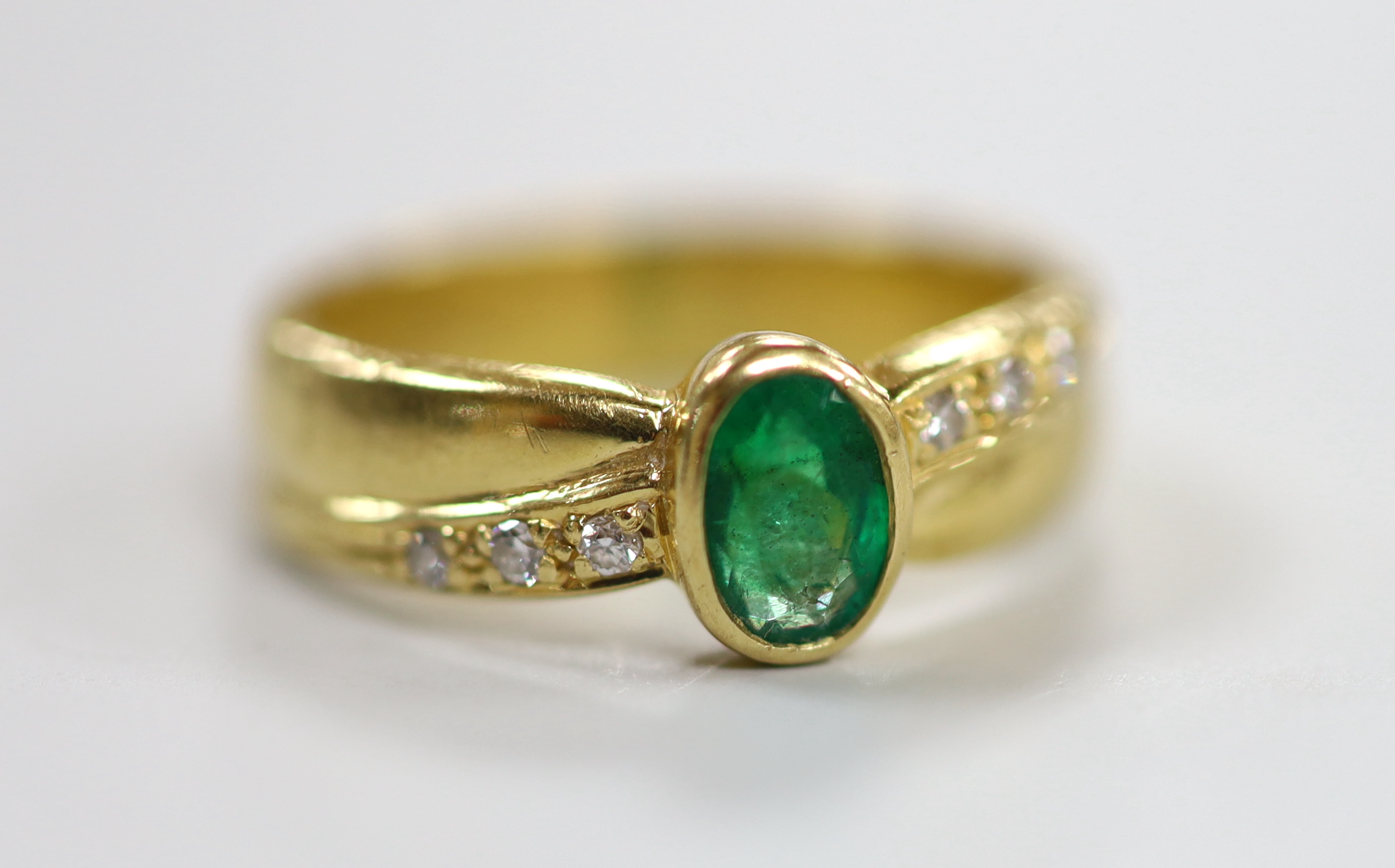 A modern 18ct gold and single stone oval cut emerald ring, with six stone diamond set shoulders, size J. gross weight 4.7 grams.                                                                                            