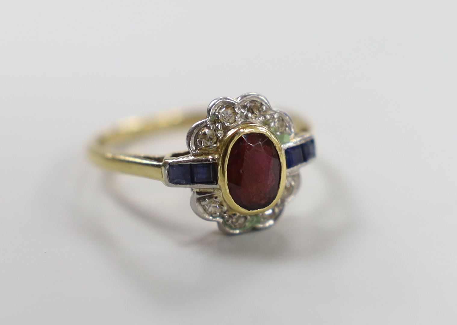 A 1920's/1930's yellow metal, ruby, sapphire and diamond set oval cluster ring, size O, gross weight 3.1 grams.                                                                                                             