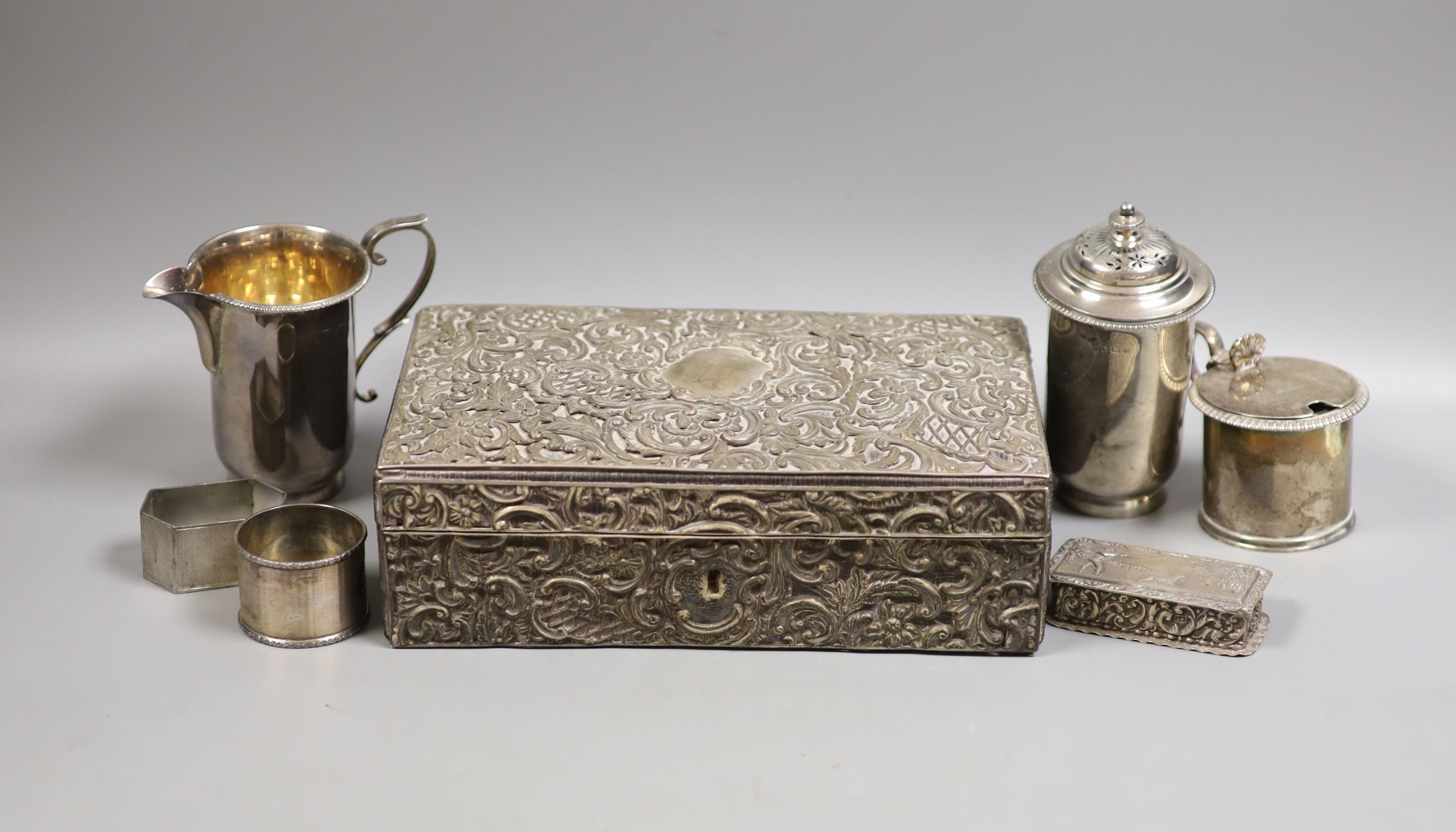 A late Victorian silver mounted leather rectangular jewellery casket, 23.2cm, a silver snuff box, the lid embossed with a wild fowling scene, a George V silver cream jug and pepper, two silver napkin rings and a Victoria
