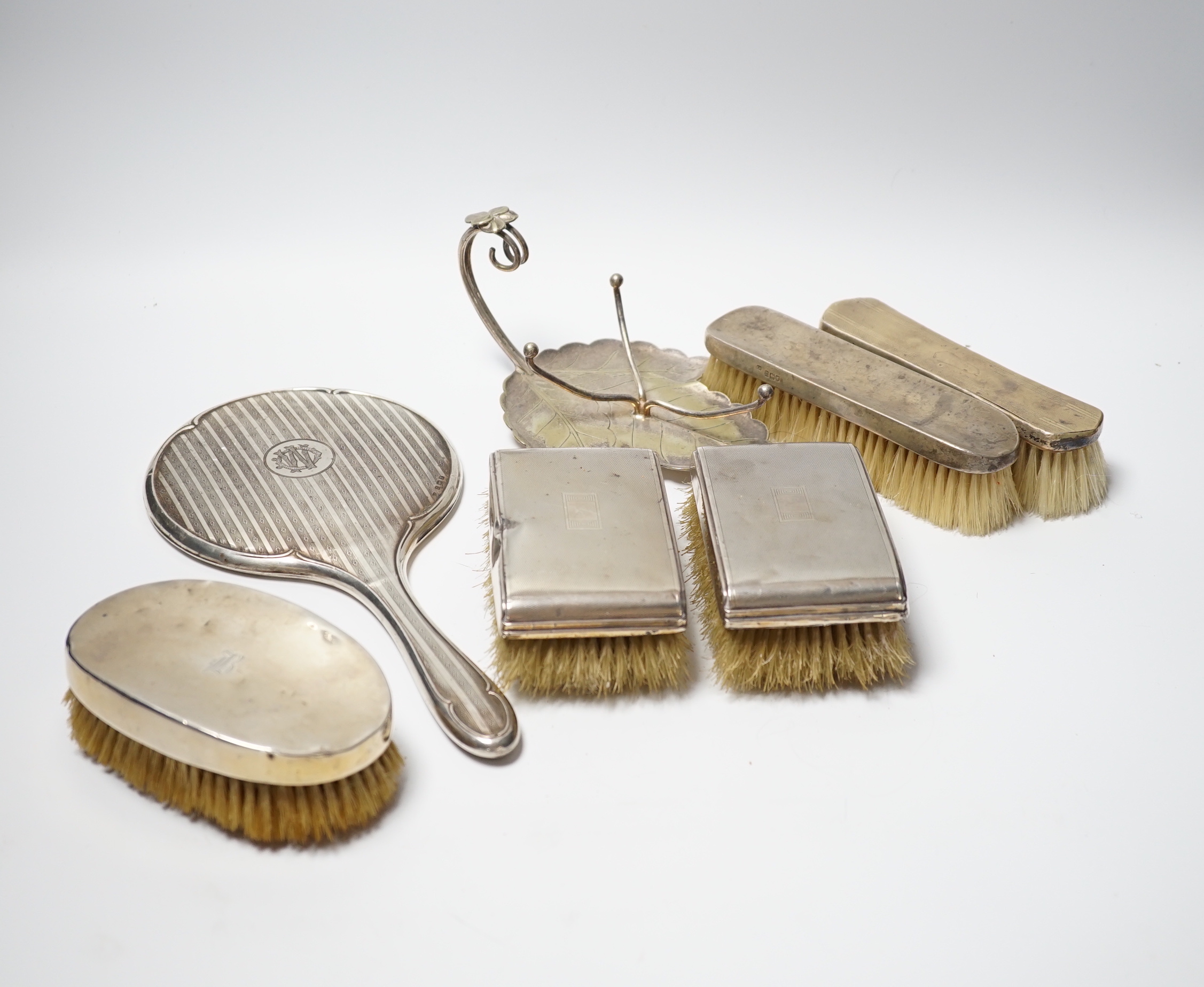 A George V silver mounted hand mirror, Birmingham, 1916, five assorted silver mounted brushes including a pair of clothes brushes and a plated stand.                                                                       