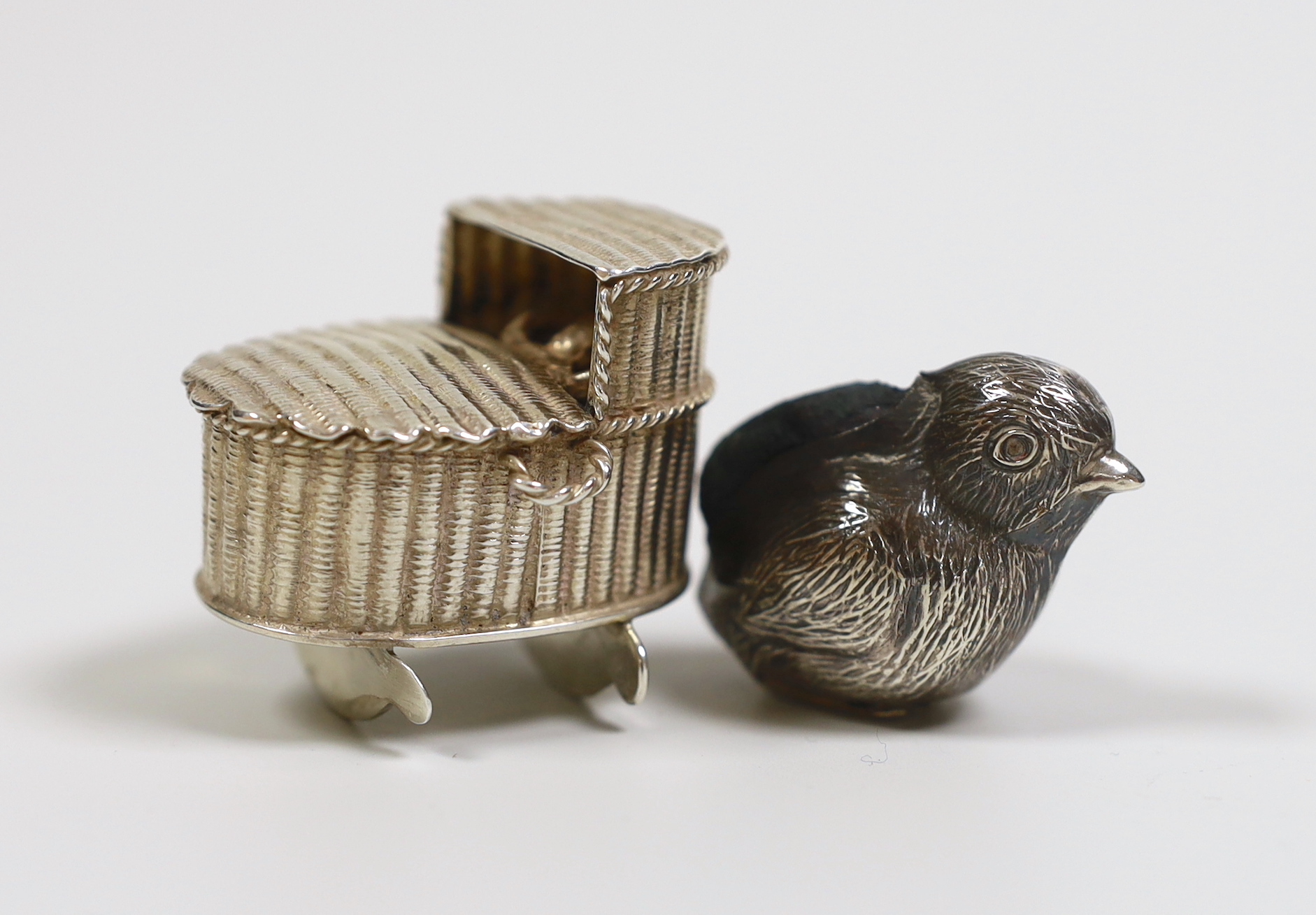 A George V silver mounted chick pin cushion, Birmingham, 1922, 39mm and a late 19th century Dutch? white metal miniature model of a child in a crib.                                                                        