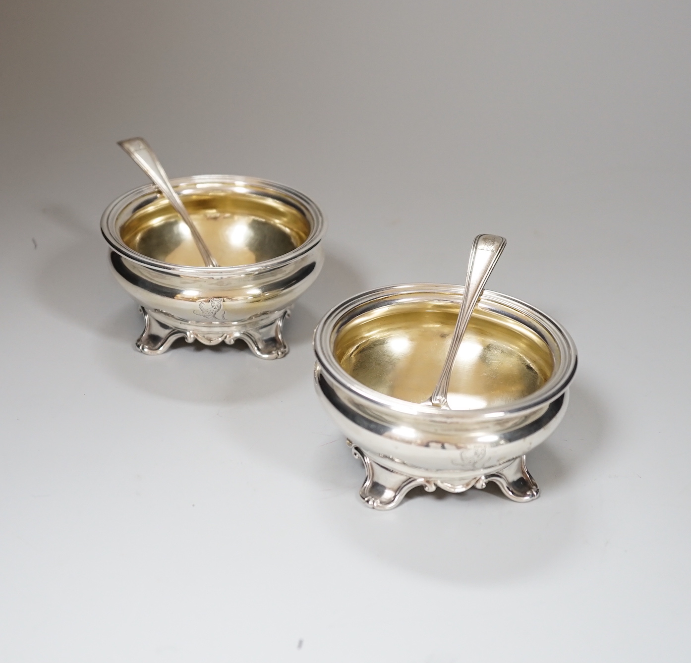 A pair of Victorian circular silver salts, with crests and scroll feet, makers Edward Barnard & Sons, London 1839, 207 grams, and a pair of George IV silver salt spoons, London 1827, 19 grams                             