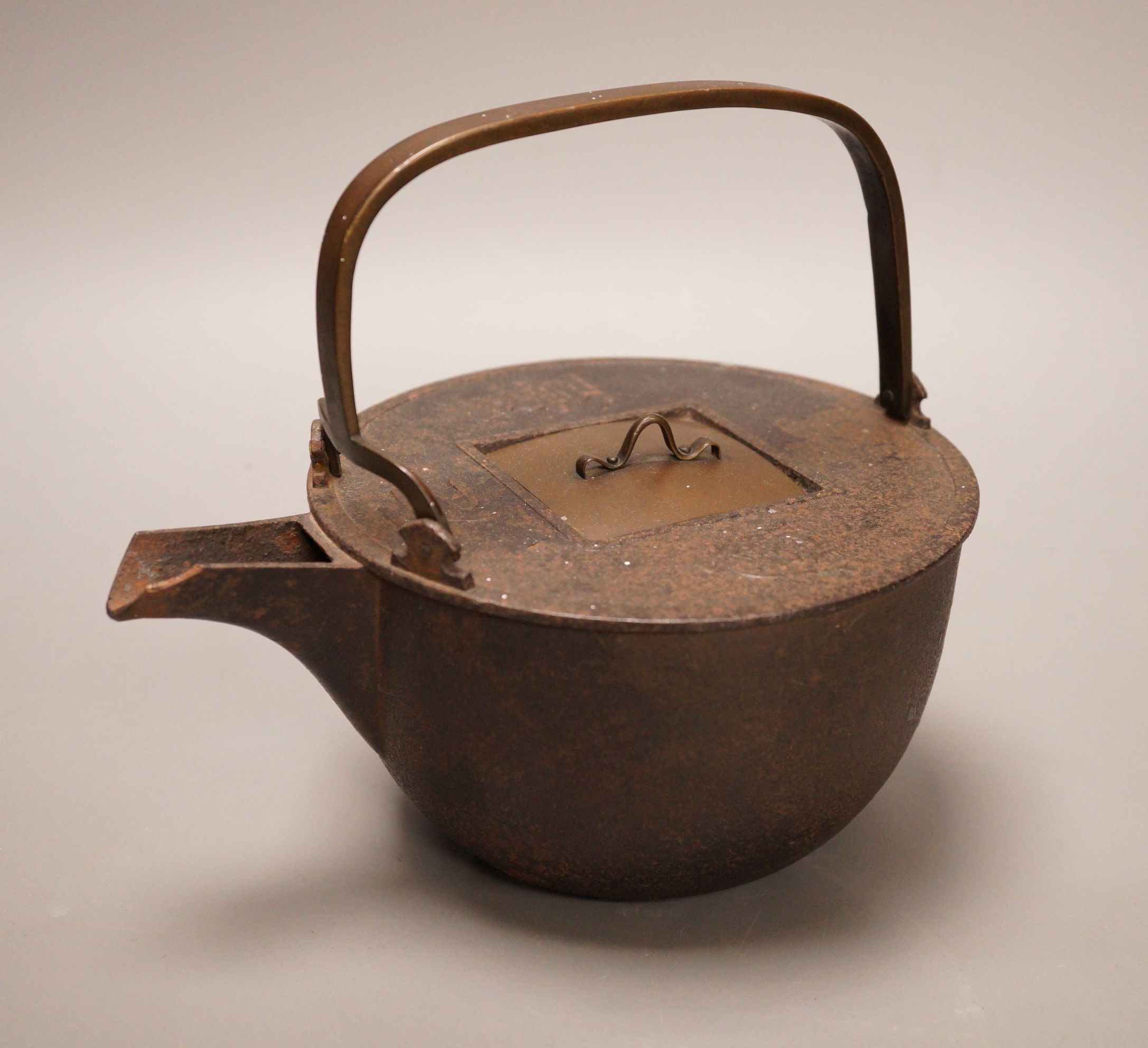 A Japanese cast iron and bronze teapot on tripod stand, inscribed, 19cm wide including spout                                                                                                                                