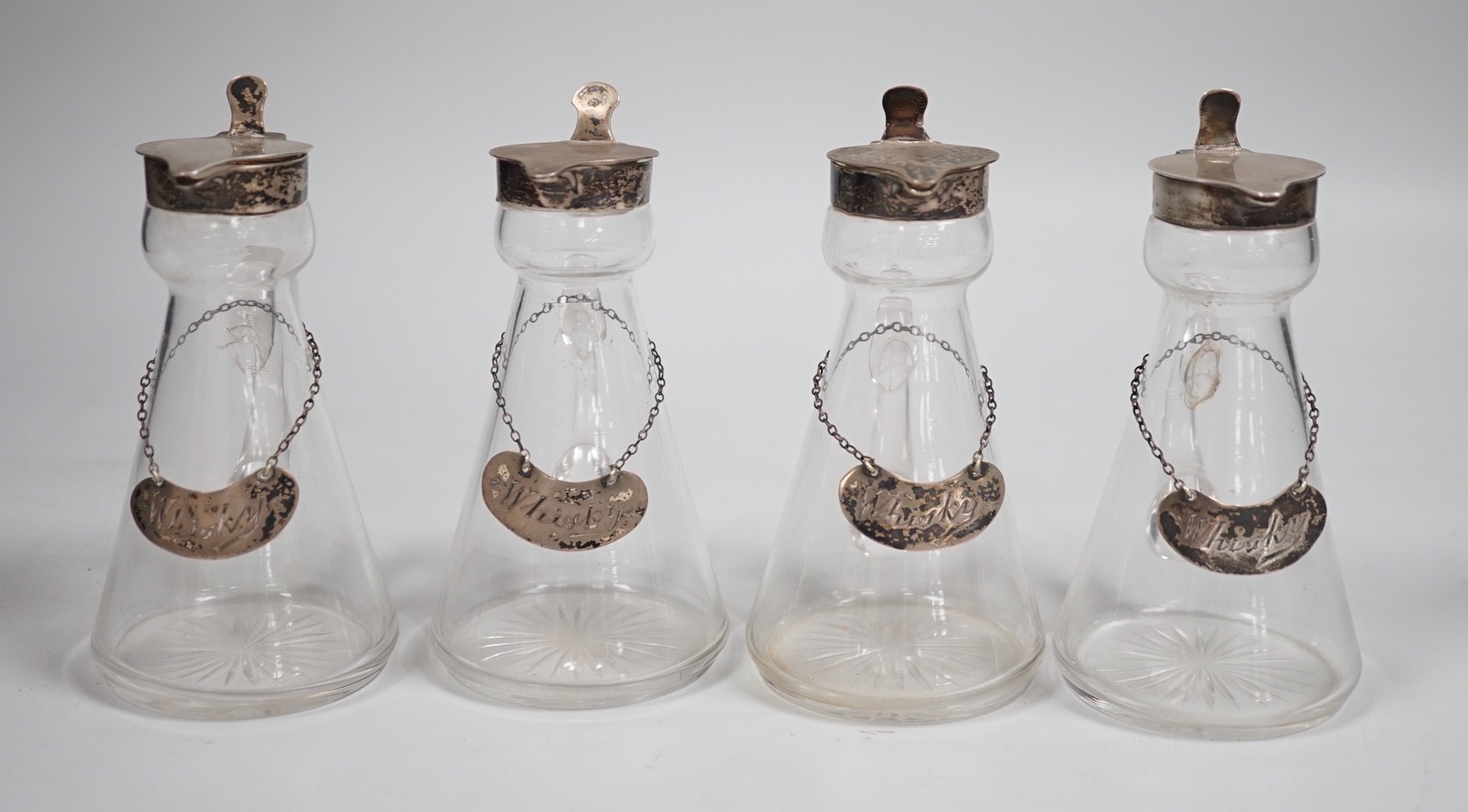 A set of four Edwardian silver mounted glass whisky noggins, H.B. Johnson & Co, Birmingham, 1909, height 12cm, together with a set of four silver whisky labels, same maker, London, 1910.                                  