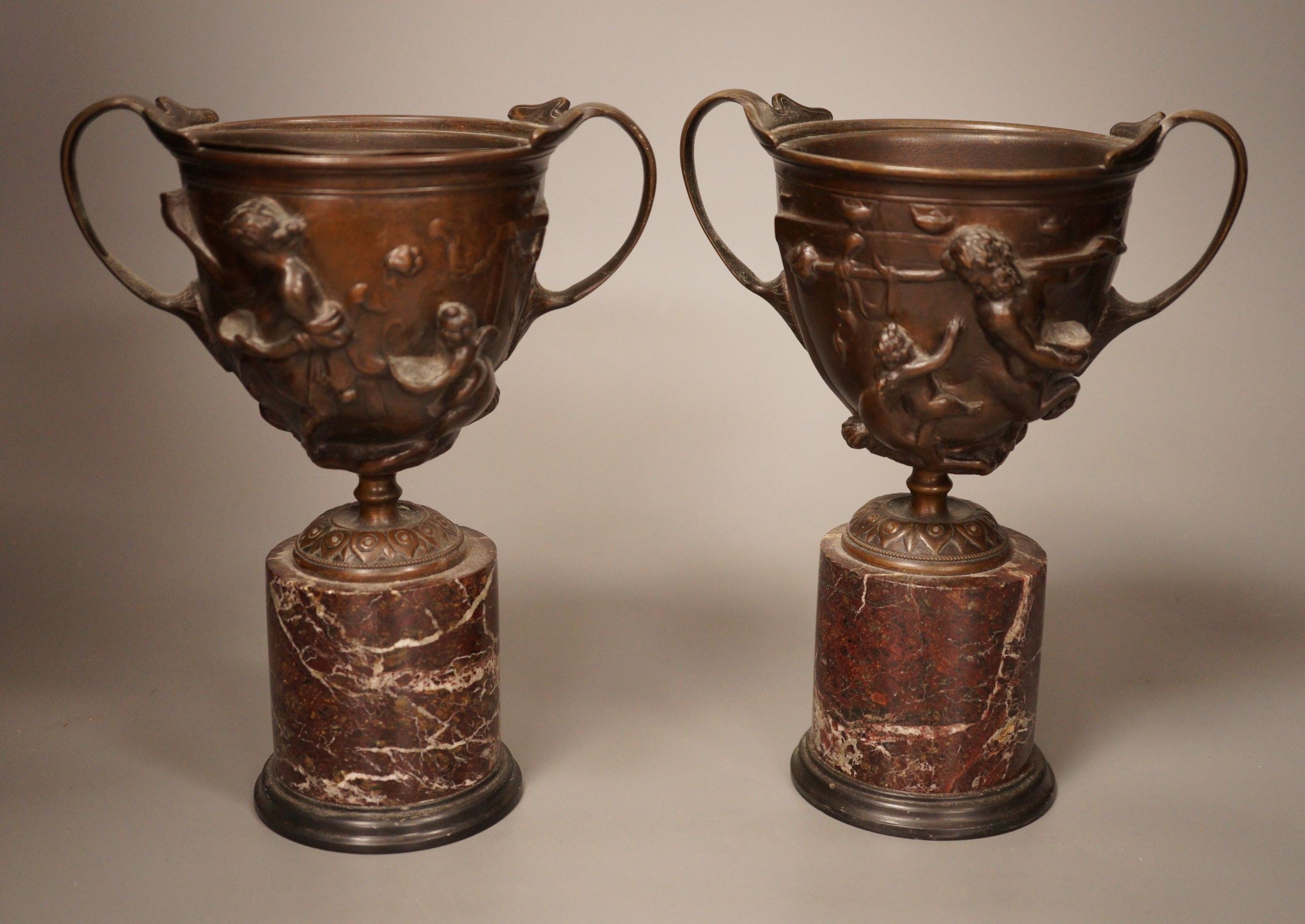 A pair of early 20th century twin handled bronze cups on marble plinth bases, 22cm                                                                                                                                          