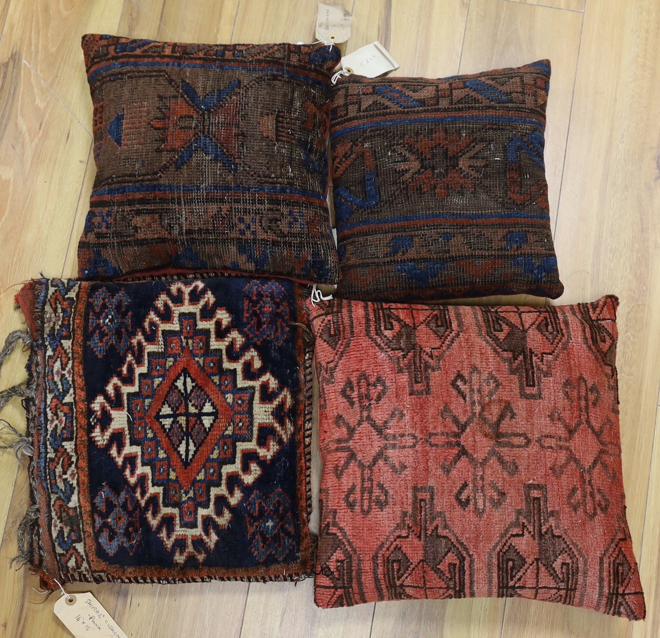 A pair of antique Persian belouch cushions, together with an Afghani Chubbash cushion, 16" x 16" and a Persian shiraz cushion, 16" x 15" (4)                                                                                
