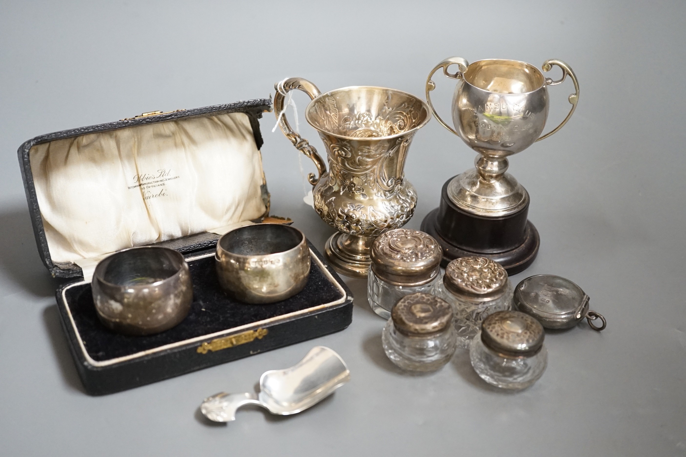 A Victorian repousse silver christening mug, Birmingham, 1861, 9.5cm, a cased pair of silver napkin rings, four assorted silver mounted toilet jars, a silver compact, small silver trophy cup and a silver caddy spoon.    