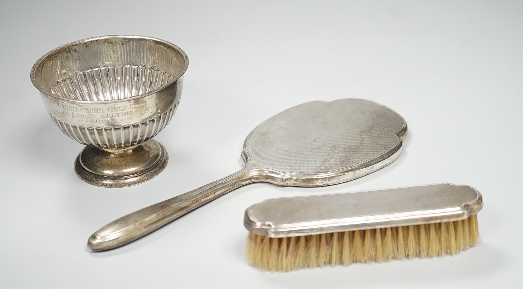 An Edwardian demi-fluted silver small presentation pedestal bowl, Sheffield, 1904, diameter 10.9cm and a silver mounted hand mirror and clothes brush.                                                                      