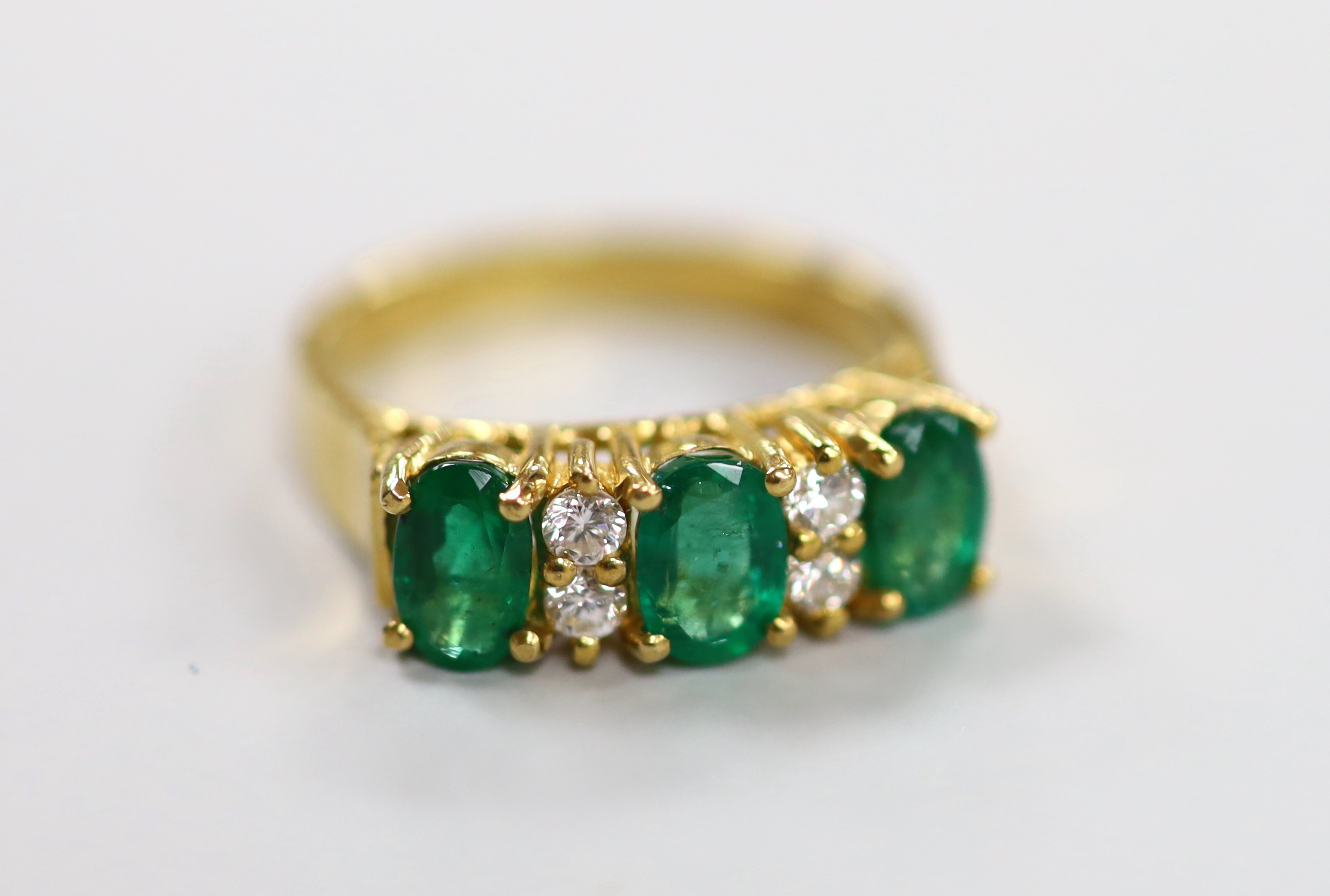 A 750 yellow metal, three stone emerald and four stone diamond spacer set half hoop ring, size K, gross weight 3.8 grams.                                                                                                   