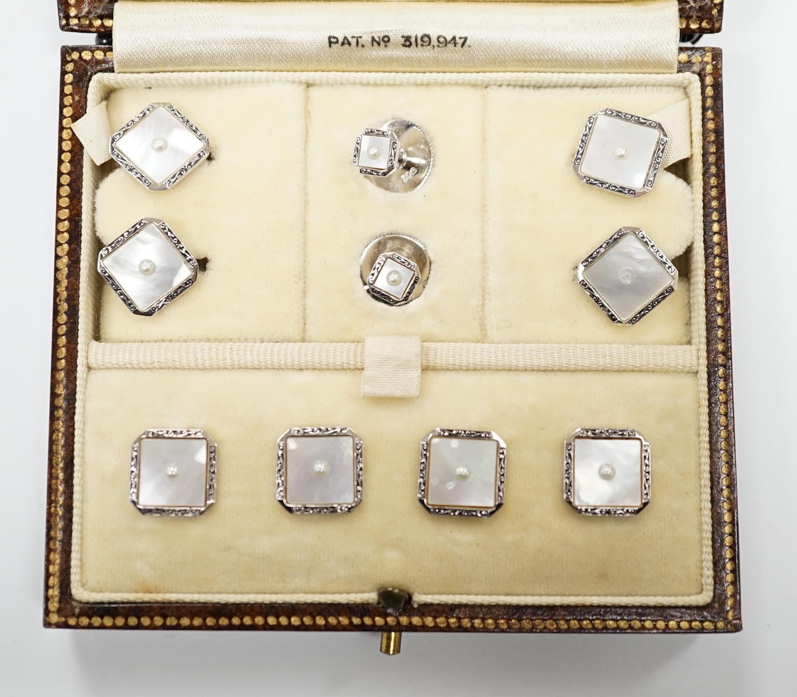 A 9ct white metal, mother of pearl and seed pearl set eight piece dress stud set, in fitted gilt tooled leather case.                                                                                                       