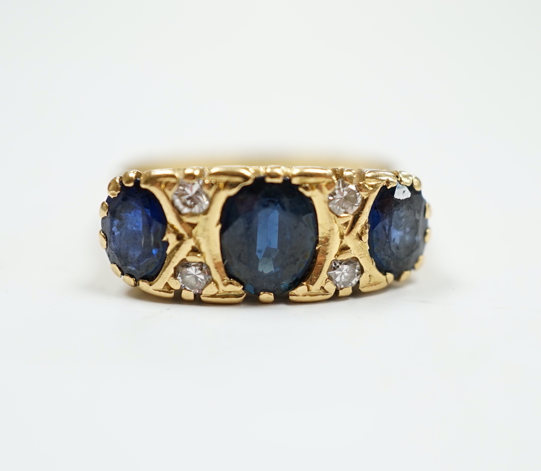 An 18ct and three stone sapphire set half hoop ring, with diamond chip spacers, size O, gross weight 6.2 grams.                                                                                                             