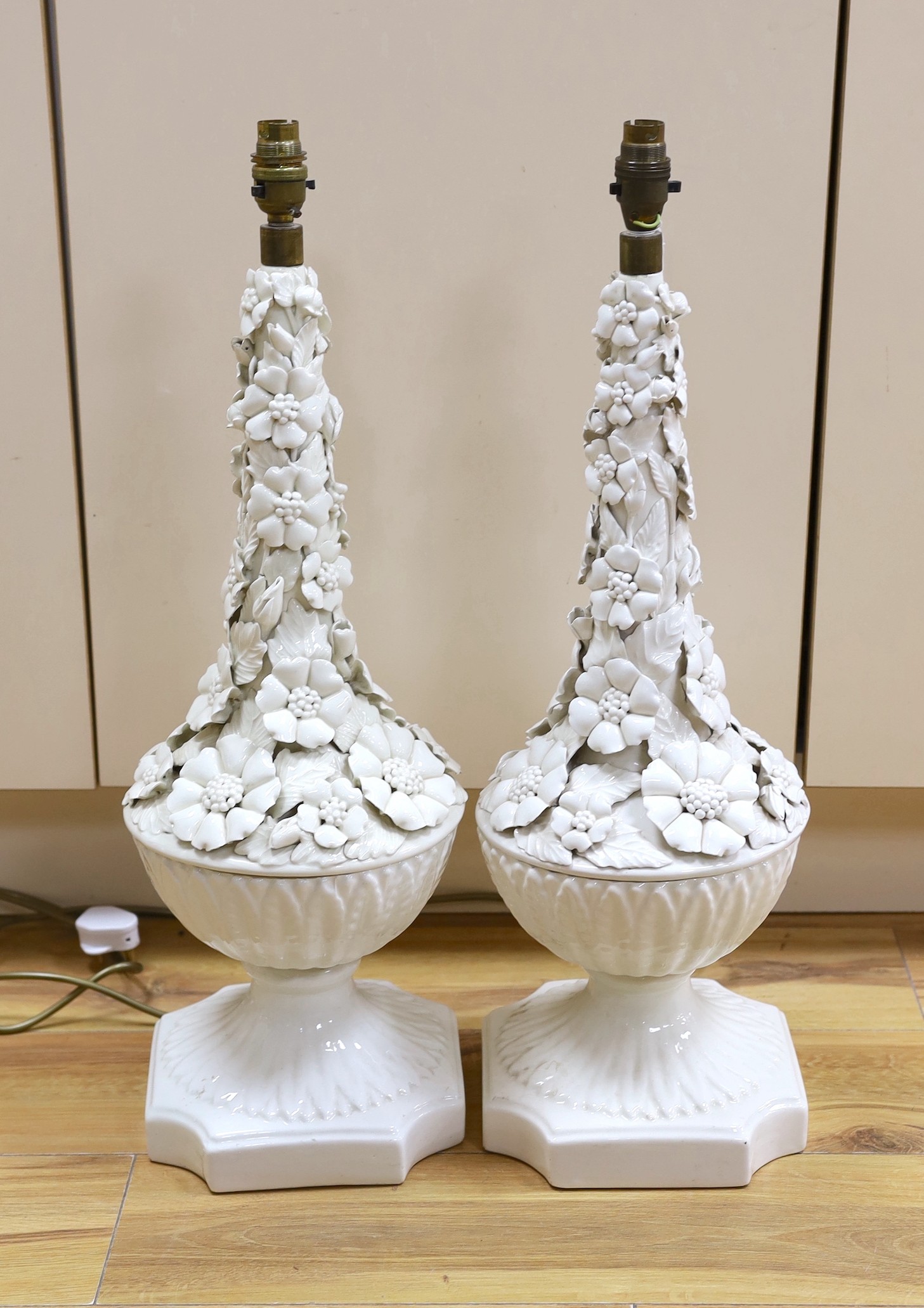 A pair of white glazed floral encrusted lamps, 58cms high not including light fitting                                                                                                                                       