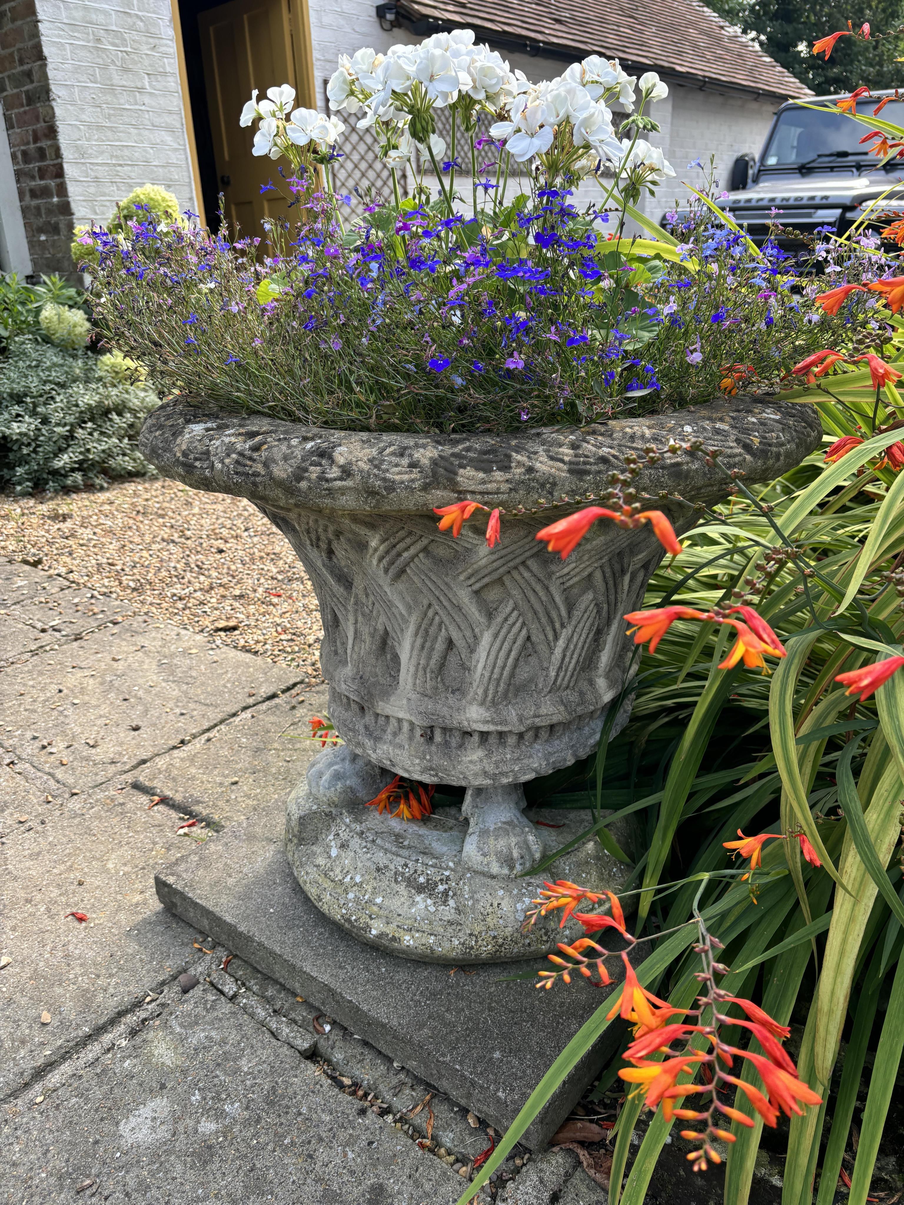 A reconstituted stone basket urn on stand, height 76cm, depth 60cm. planting removed, Condition - weathered, otherwise good                                                                                                 