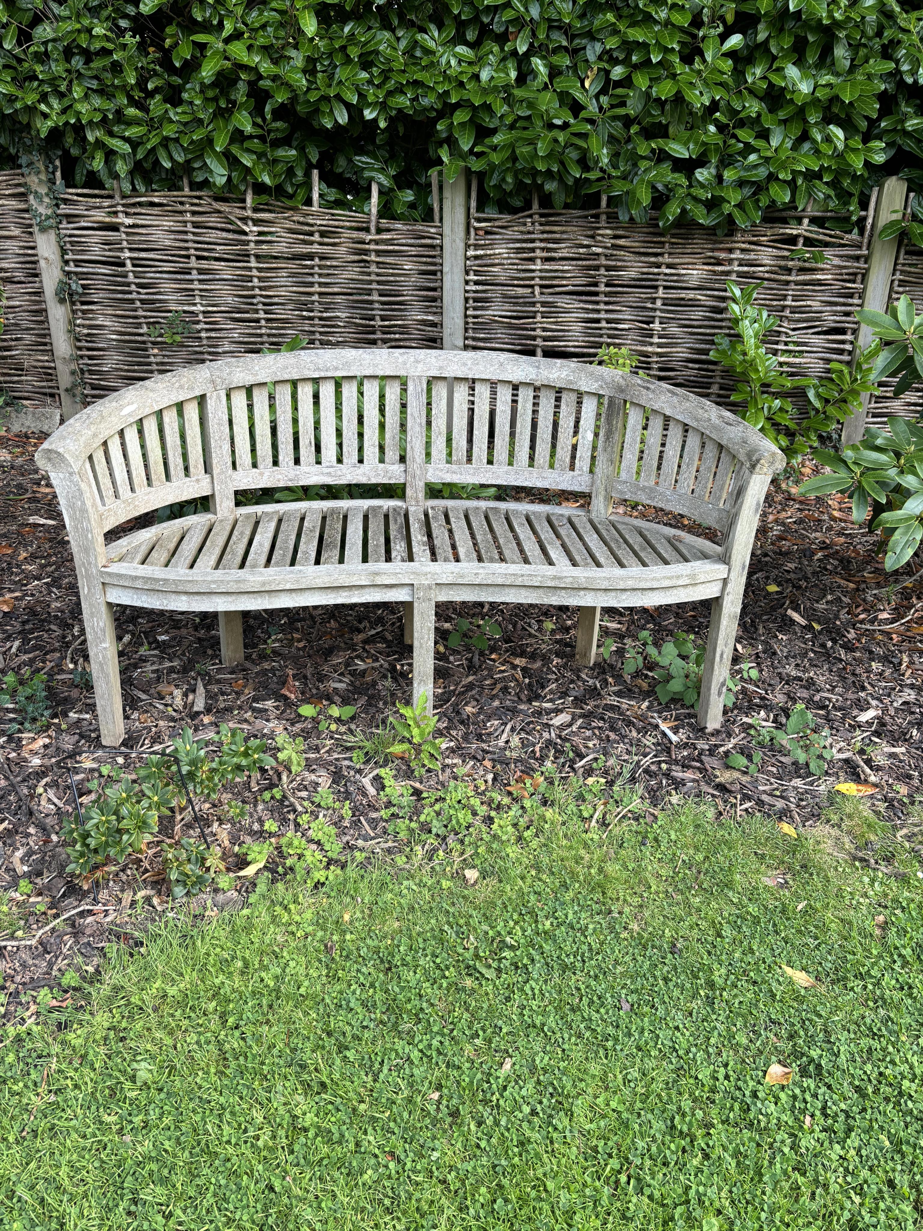 A curved teak bench, 160cm, 82cm high. Condition - weathered, otherwise good                                                                                                                                                