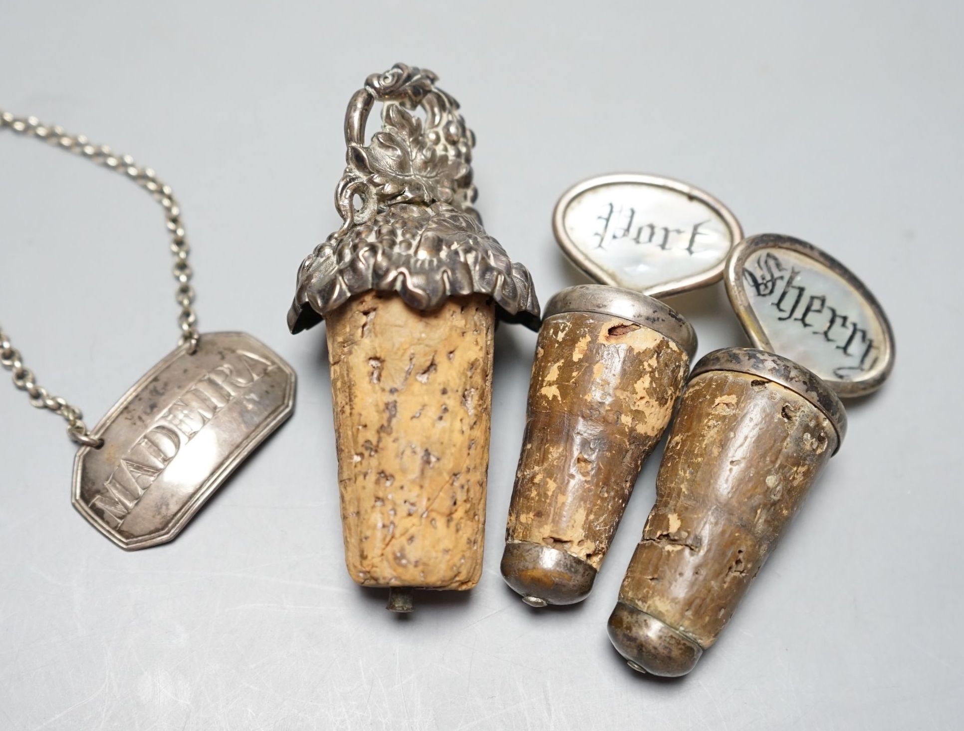 A George III silver 'Madeira' wine label, London, 1803 and three mounted cork bottle stoppers.                                                                                                                              