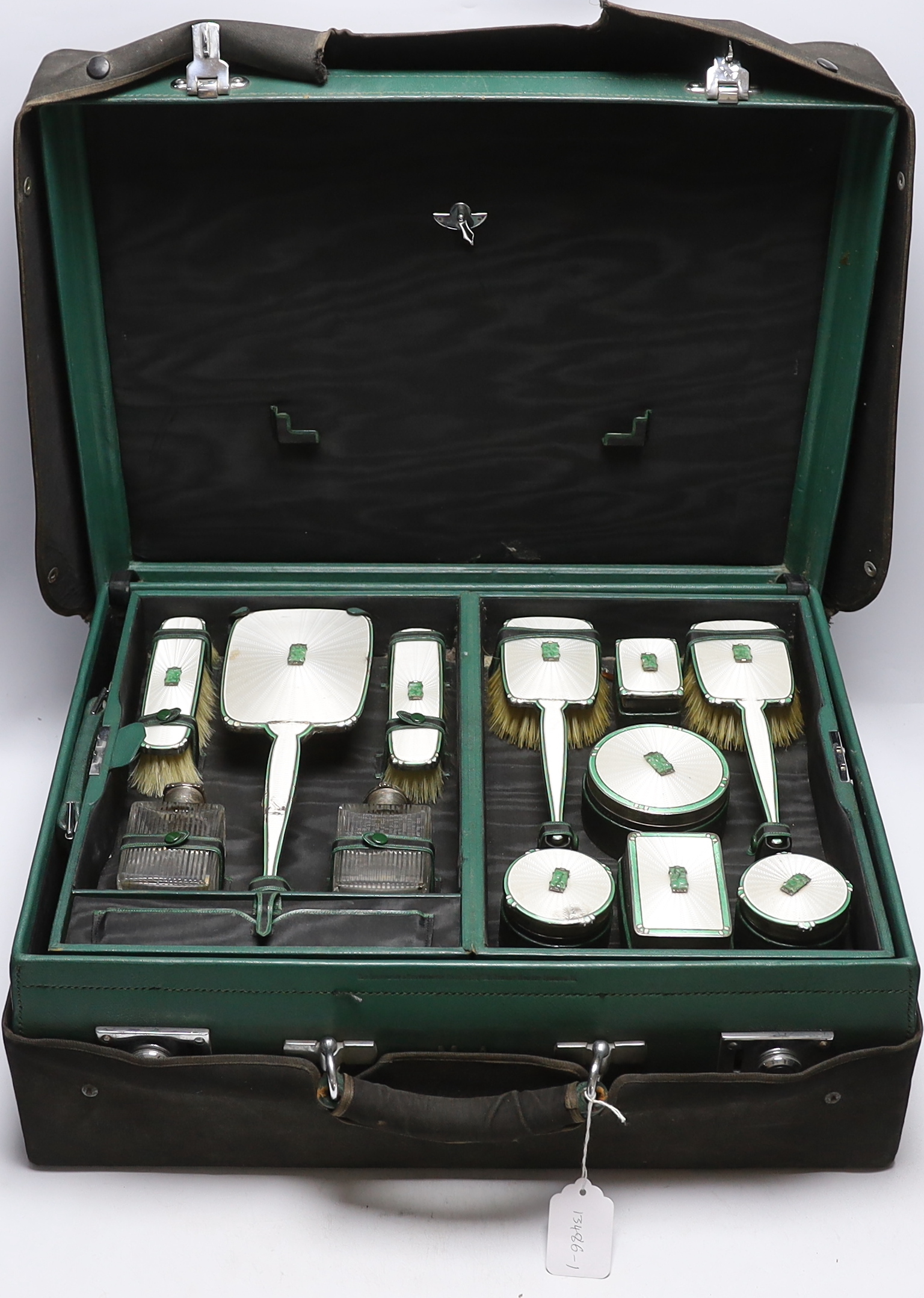 A George V silver, enamel and Chinese jadeite mounted twelve piece dressing table set, Goldsmiths & Silversmiths Co Ltd, Birmingham, 1936, housed in green leather travelling case, case width 53cm (a.f.).                 