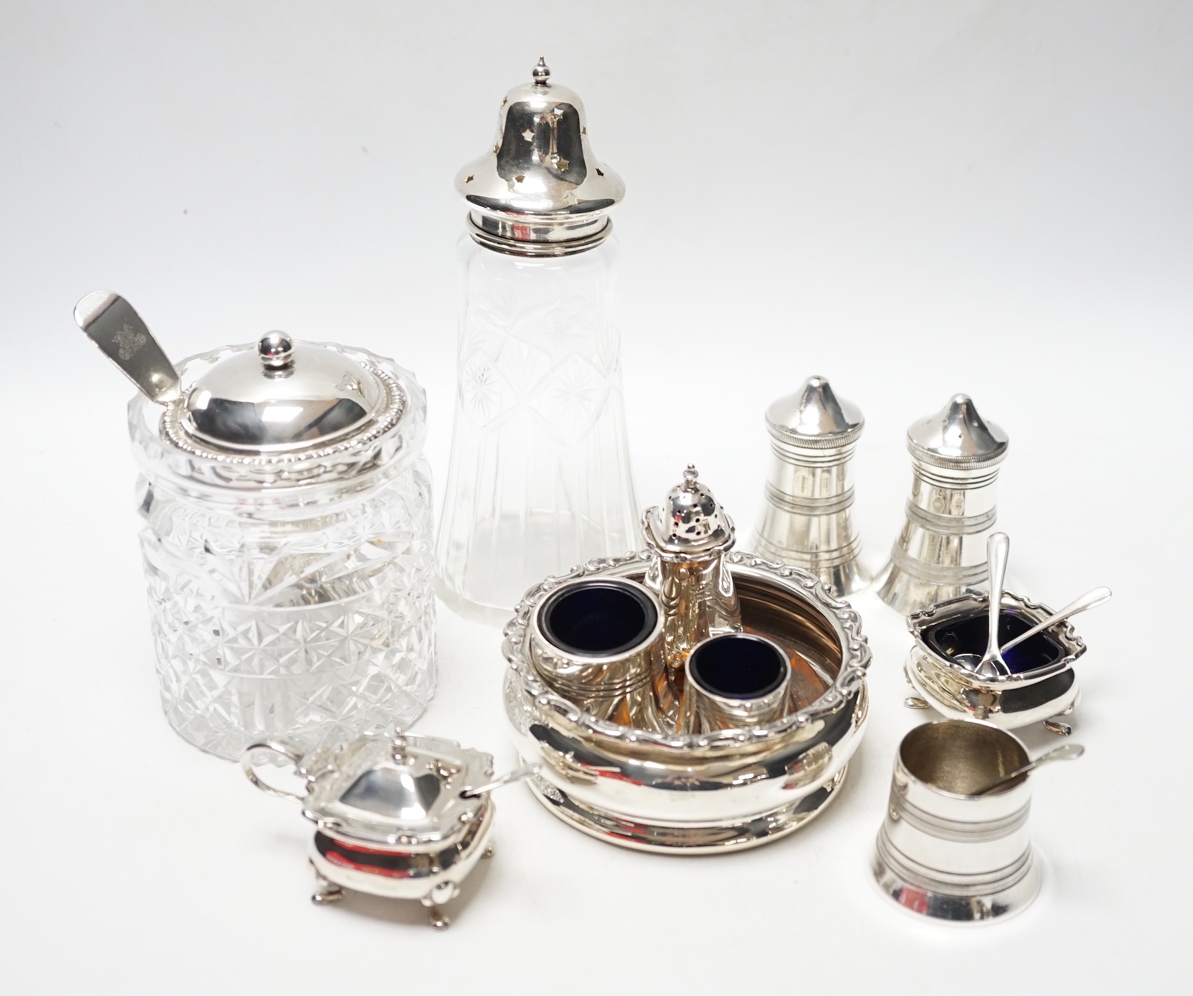 An Edwardian silver wine coaster, William Hutton & Sons, Birmingham, 1903, diameter 10.4cm, a later silver three piece condiment set, a silver mounted glass preserve jar, with a George silver teaspoon and six plated item