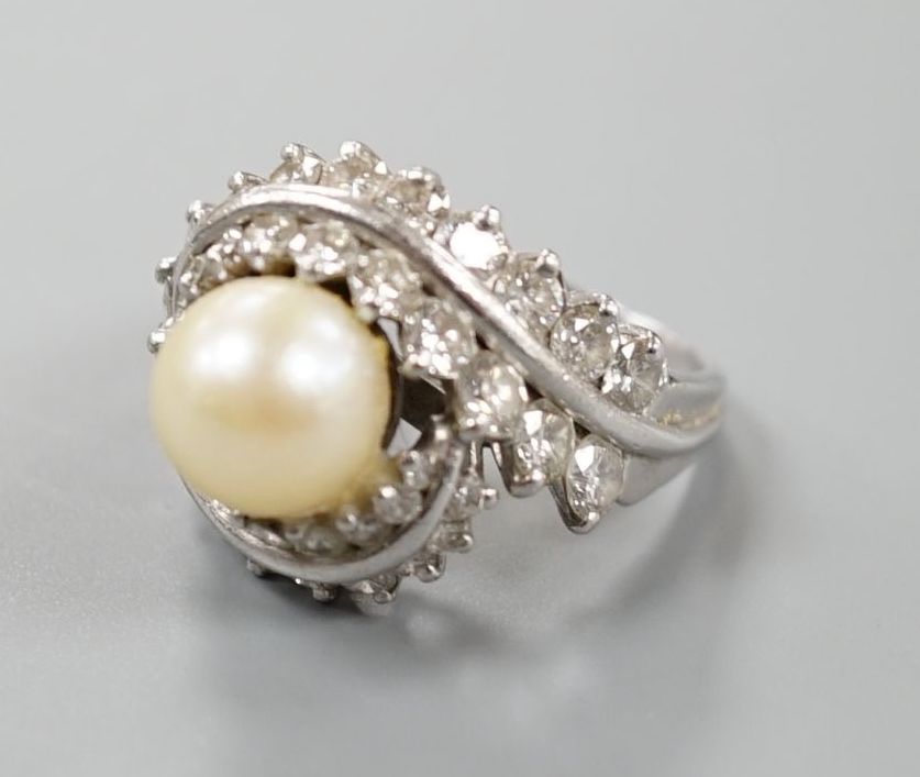 A white metal single stone cultured pearl and diamond cluster set scroll dress ring, size Q, gross weight 13.6 grams.                                                                                                       