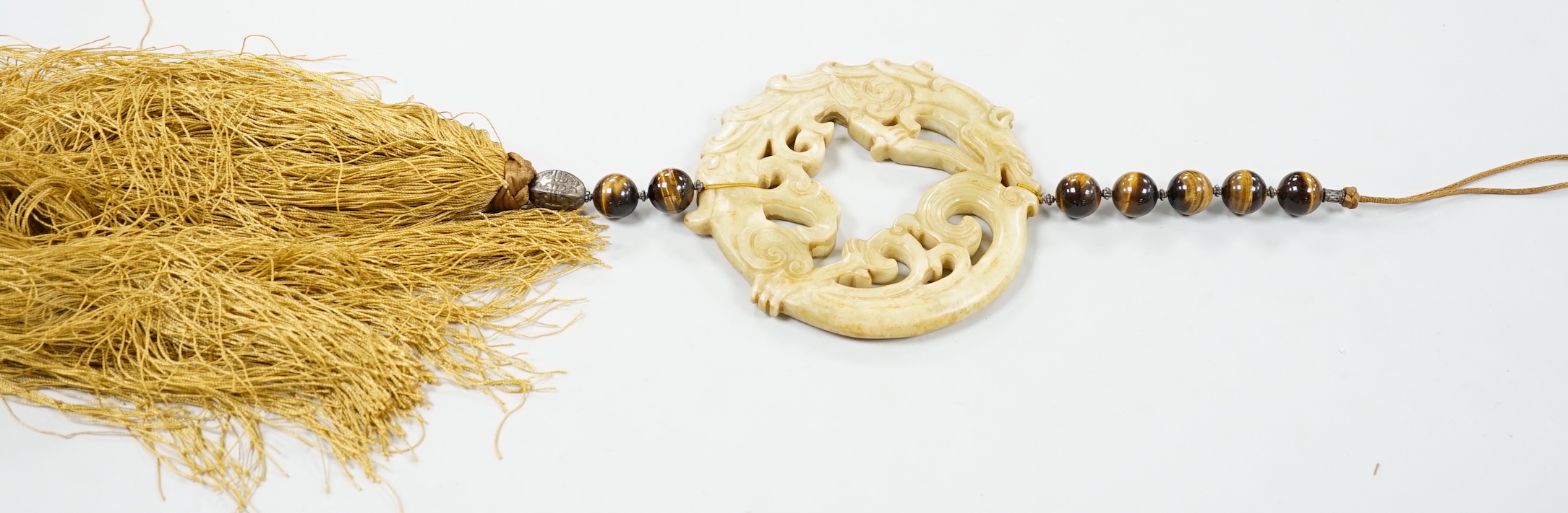 A large Chinese bowenite jade disc, threaded with tiger's eye beads and long silk tassel, 90cm long                                                                                                                         