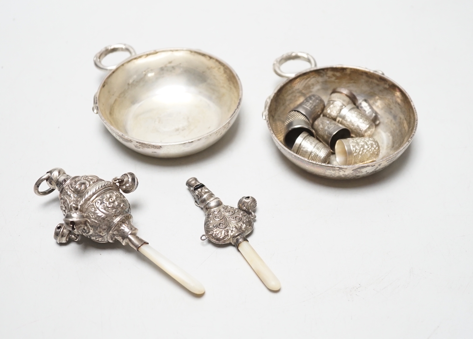 A pair of George V silver taste vin, D & J Welby Ltd, diameter 82mm, a late Victorian mother of pearl handled repousse silver child's rattle, one other larger similar silver rattle and eight thimbles including five silve