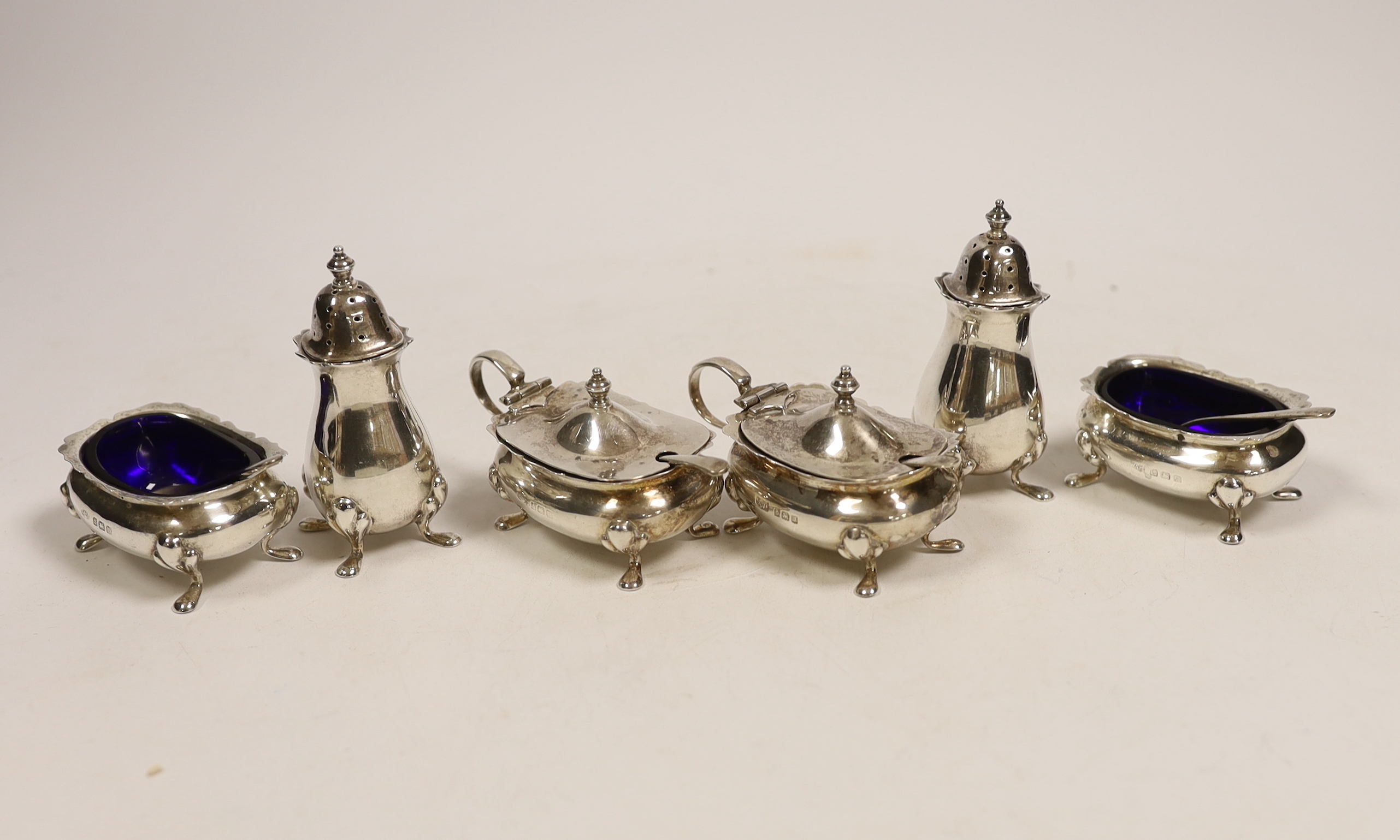 A George V silver three piece condiment set, Adie Brothers, Birmingham, 1928 and two matching spoons, together with a matched three piece silver condiment set and two silver spoons.                                       