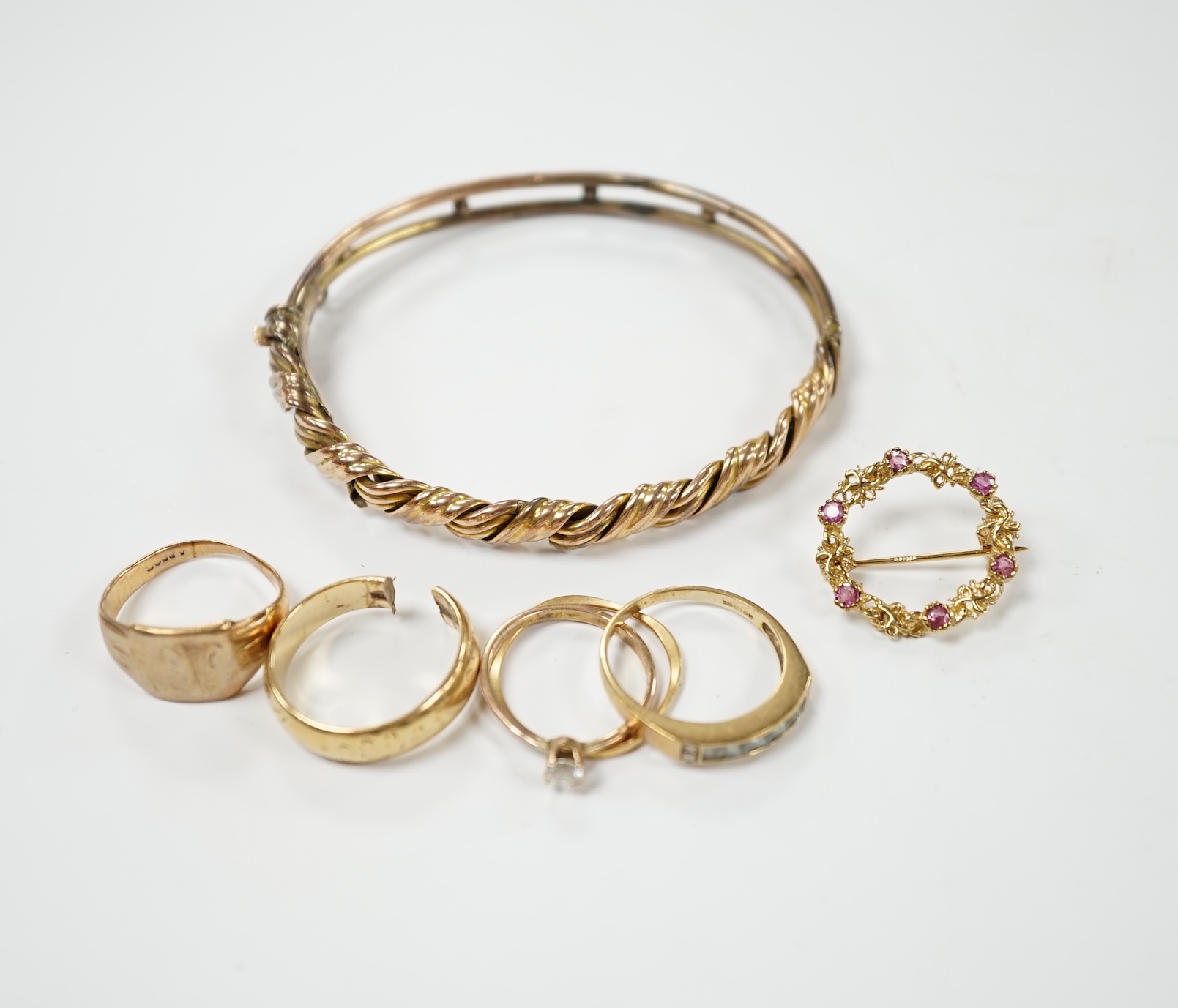 An early 20th century 9ct hinged bangle, three assorted 9ct gold rings and a modern 9ct gold and gem set brooch and two other yellow metal rings, gross weight 23.2 grams. Condition - poor                                 