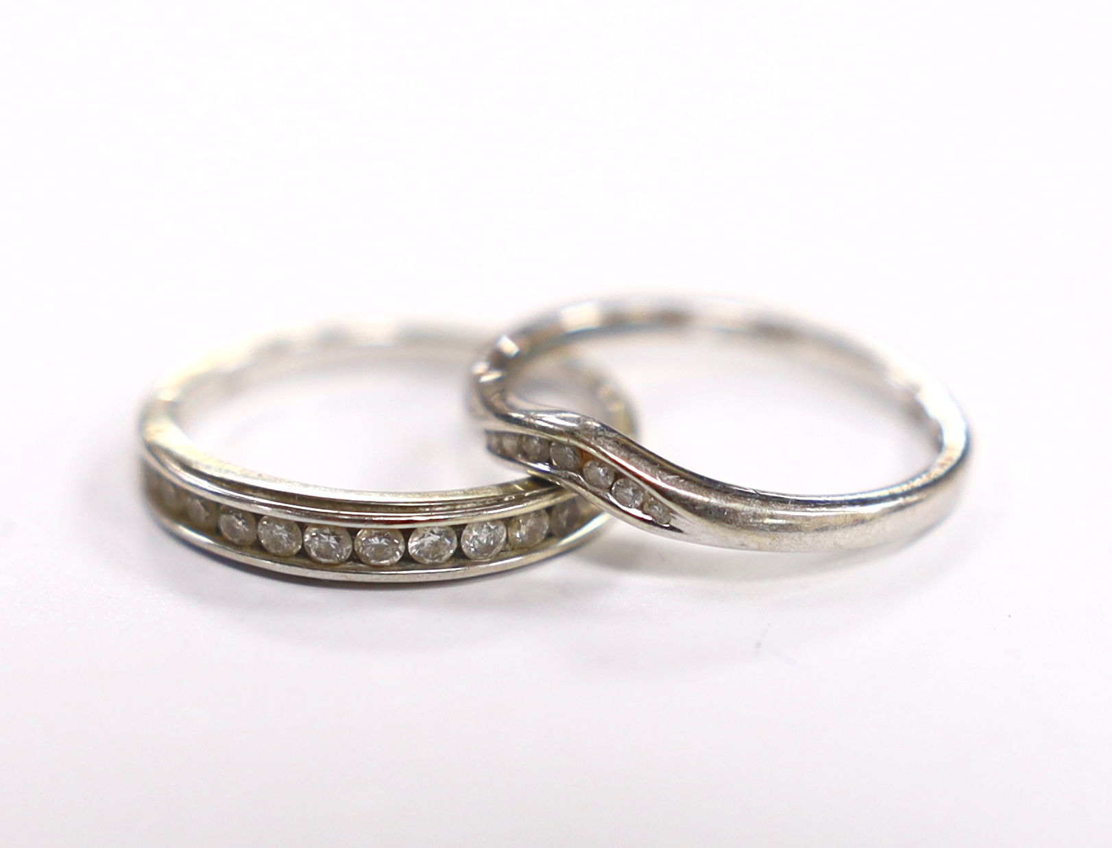 A modern 9ct white gold and diamond chip set half eternity ring, size M and a similar 9ct gold part curved channel set diamond ring, size N, gross weight 3.5 grams.                                                        