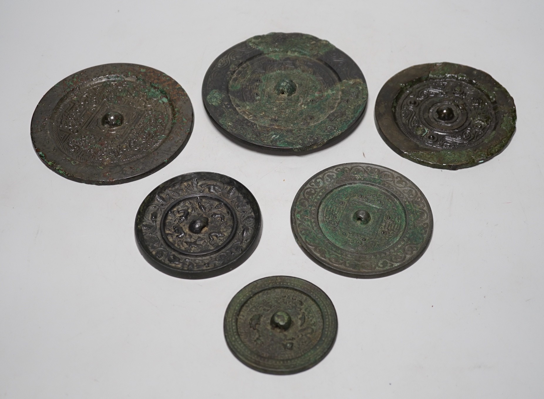 A group of six Chinese archaic bronze mirrors, including two Han dynasty TLV mirrors, and a Tang dynasty squirrel and vine small mirror, five corroded, largest 14cm diameter                                               