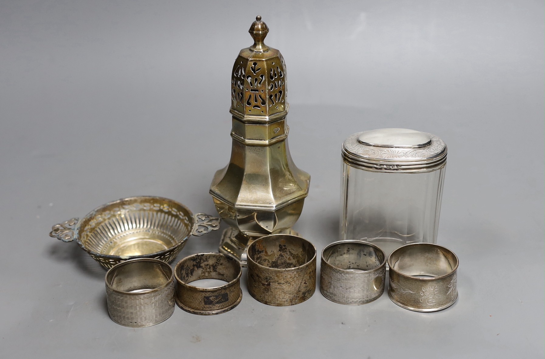 A George V silver sugar caster, London, 1933, 17cm, a silver topped glass toilet jar, a silver bon bon dish and five silver serviette rings.                                                                                