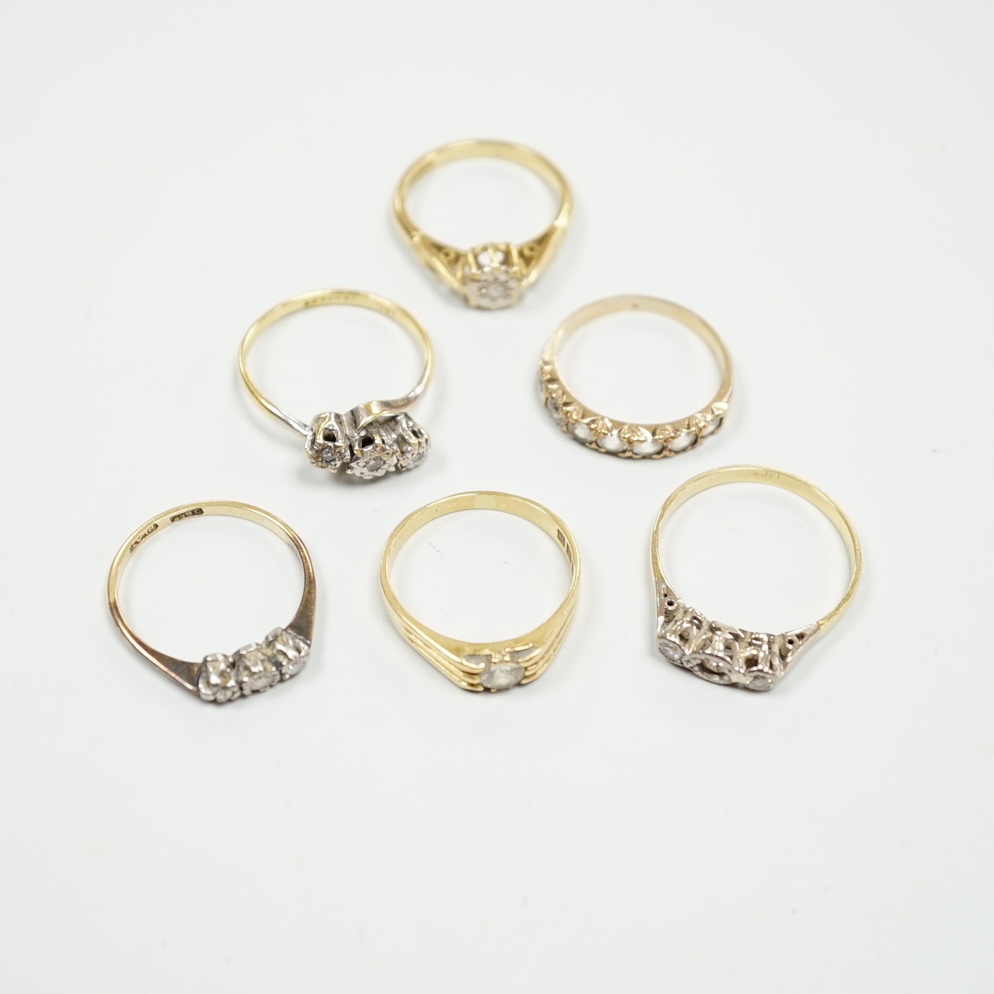 Six assorted gold dress rings, comprising an 18ct gold and platinum three stone ring, size O, an 18ct gold claw set solitaire diamond ring, size O, an 18ct gold illusion set solitaire diamond ring, size L, an 18ct gold t