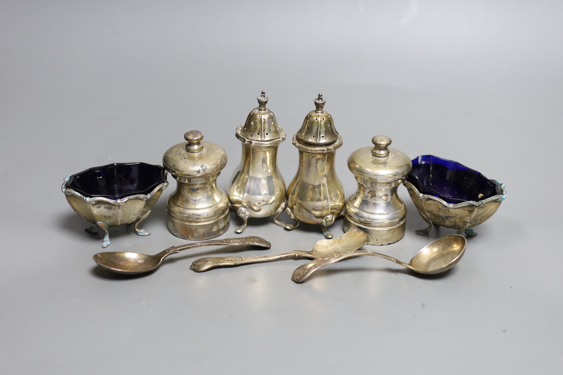 A modern pair of silver capstan shaped pepper mills, a pair of silver salts and pepper pots, a pair of matching salts and three various spoons.                                                                             