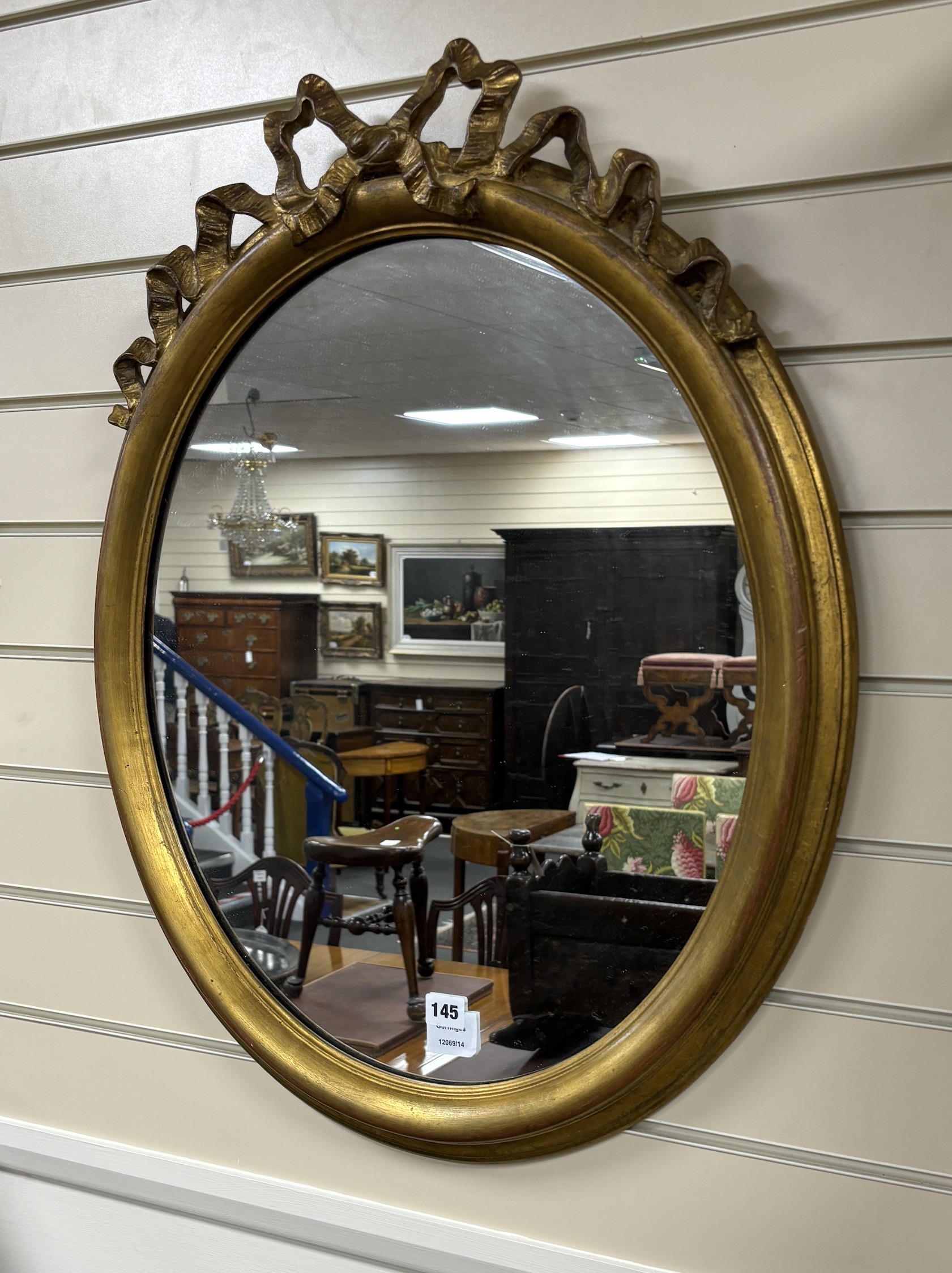 An oval giltwood and composition wall mirror with ribbon fold pediment, width 60cm, height 74cm                                                                                                                             