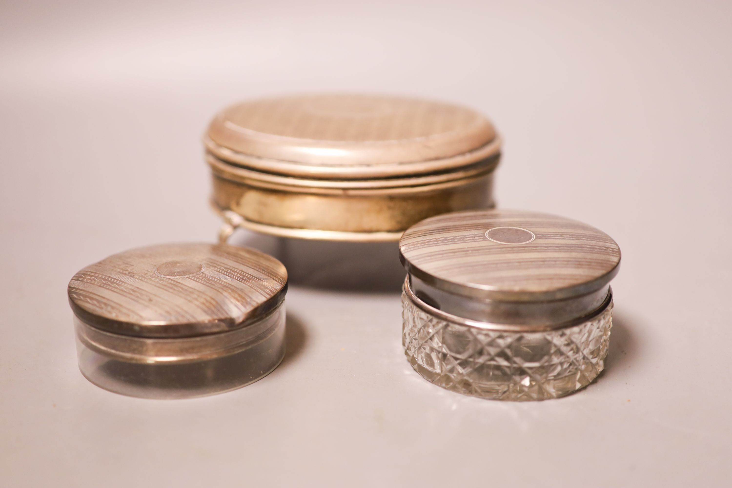 An Edwardian silver oval trinket box, William Comyns, London, 1909, 12.4cm and two round silver mounted glass toilet boxes.                                                                                                 