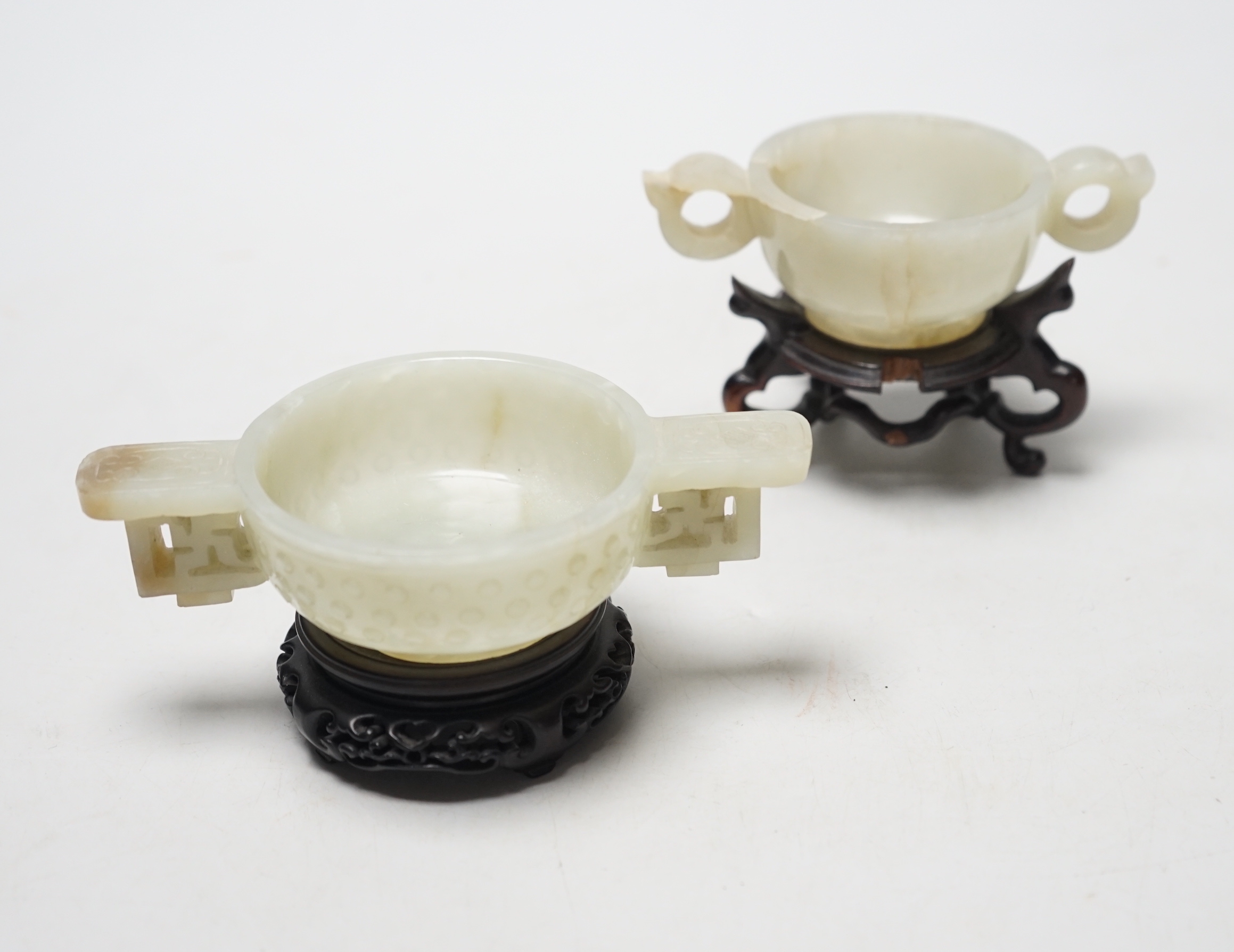 Two Chinese pale celadon jade cups, Qing dynasty, on carved hardwood stands, largest 13cm wide                                                                                                                              